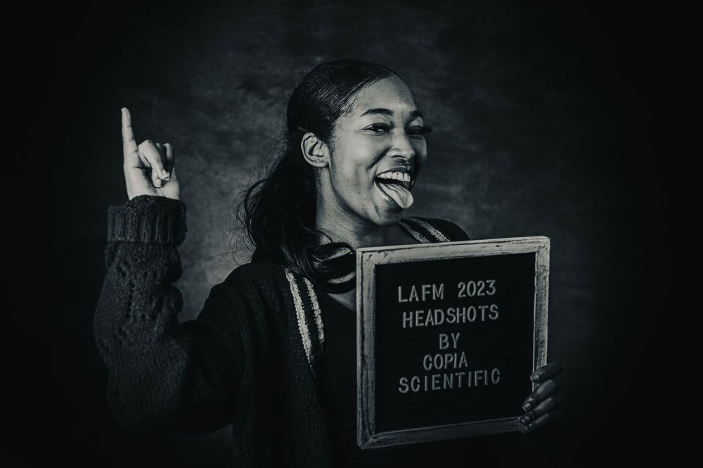 Woman laughing and posing with LAFM 2023 Headshots by Ooma Scientific sign in black and white photo.