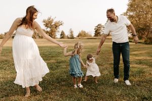 Family of four holding hands and playing together in a green field during golden hour outdoor photo session.