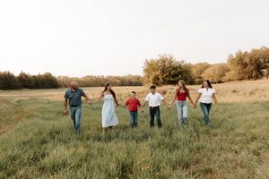 Family of six holding hands walking through a green field at golden hour in a candid outdoor portrait.