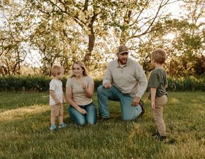 Family of four enjoying a sunny outdoor moment on green grass with trees in the background.