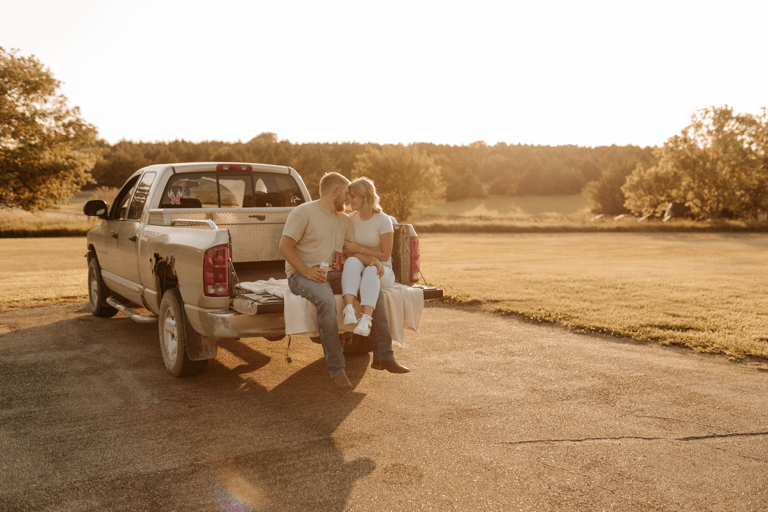 Couple sitting on truck tailgate at golden hour in a rural field at sunset.