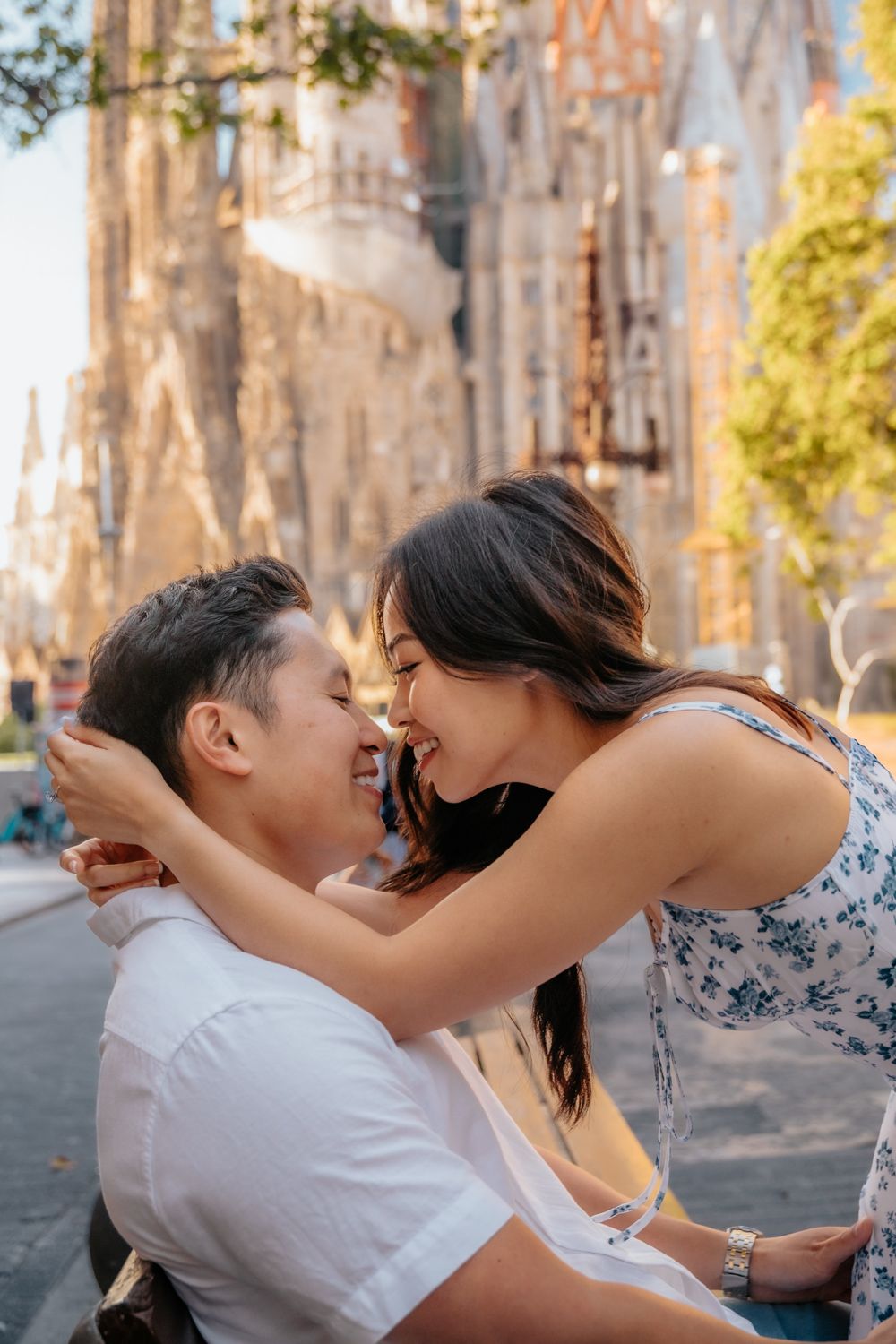 A romantic engagement photo of a couple standing by the Plaça de Gaudí pond, with the stunning reflection of the Sagrada Família behind them