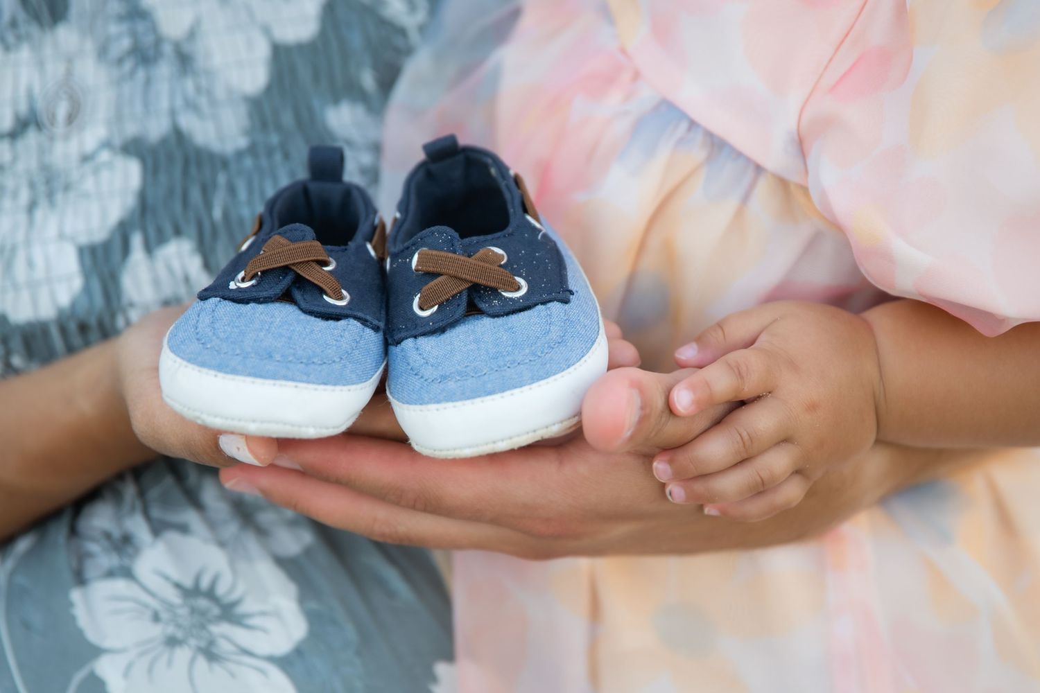 Pregnant woman in purple sweater with husband's hands resting on baby bump, both wearing wedding rings.