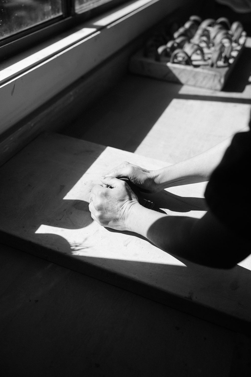Black and white photo of hands drawing on paper in sunlight near a window.