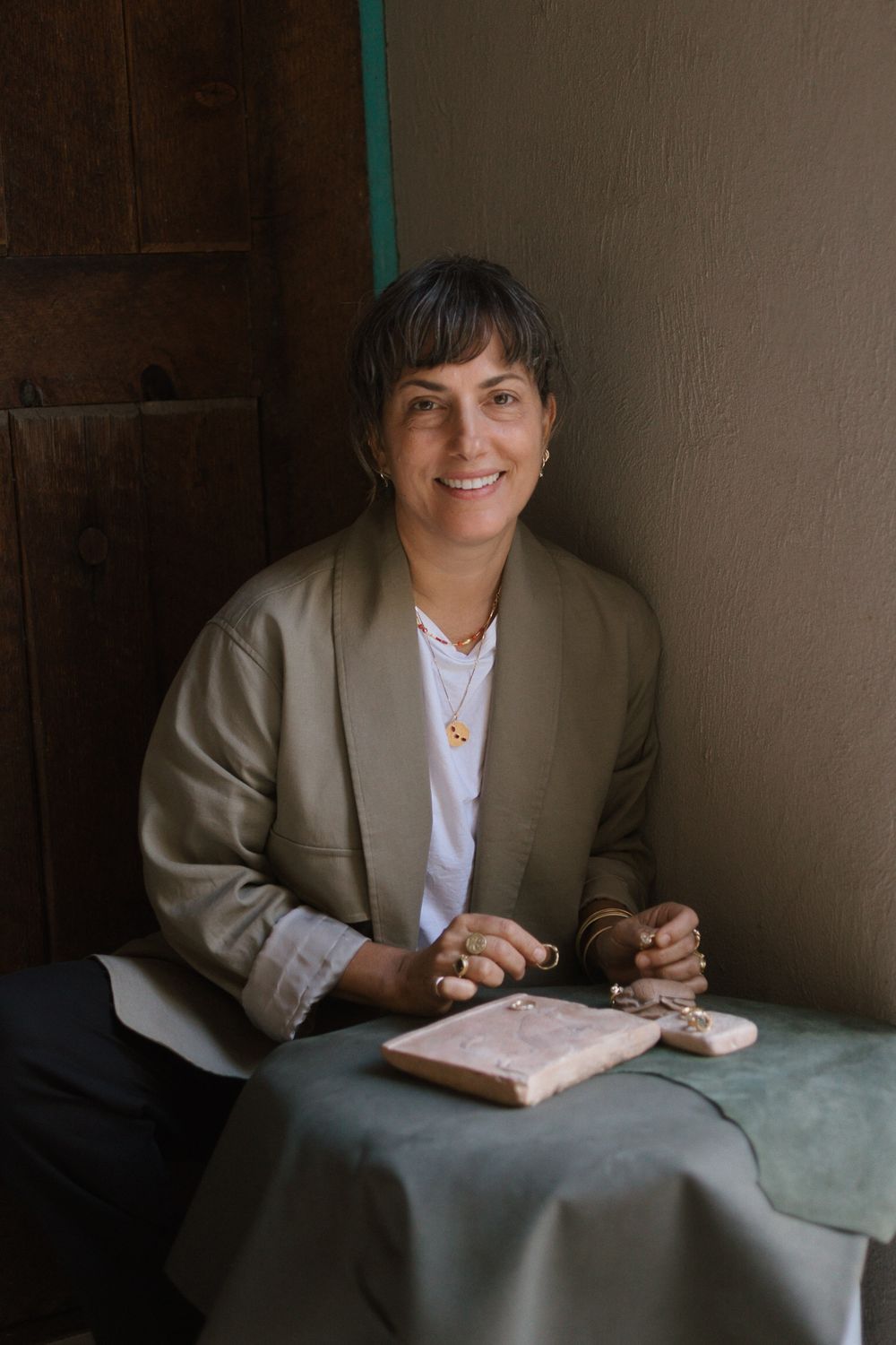 Smiling woman in sage blazer sitting at table with pink marble jewelry tray.