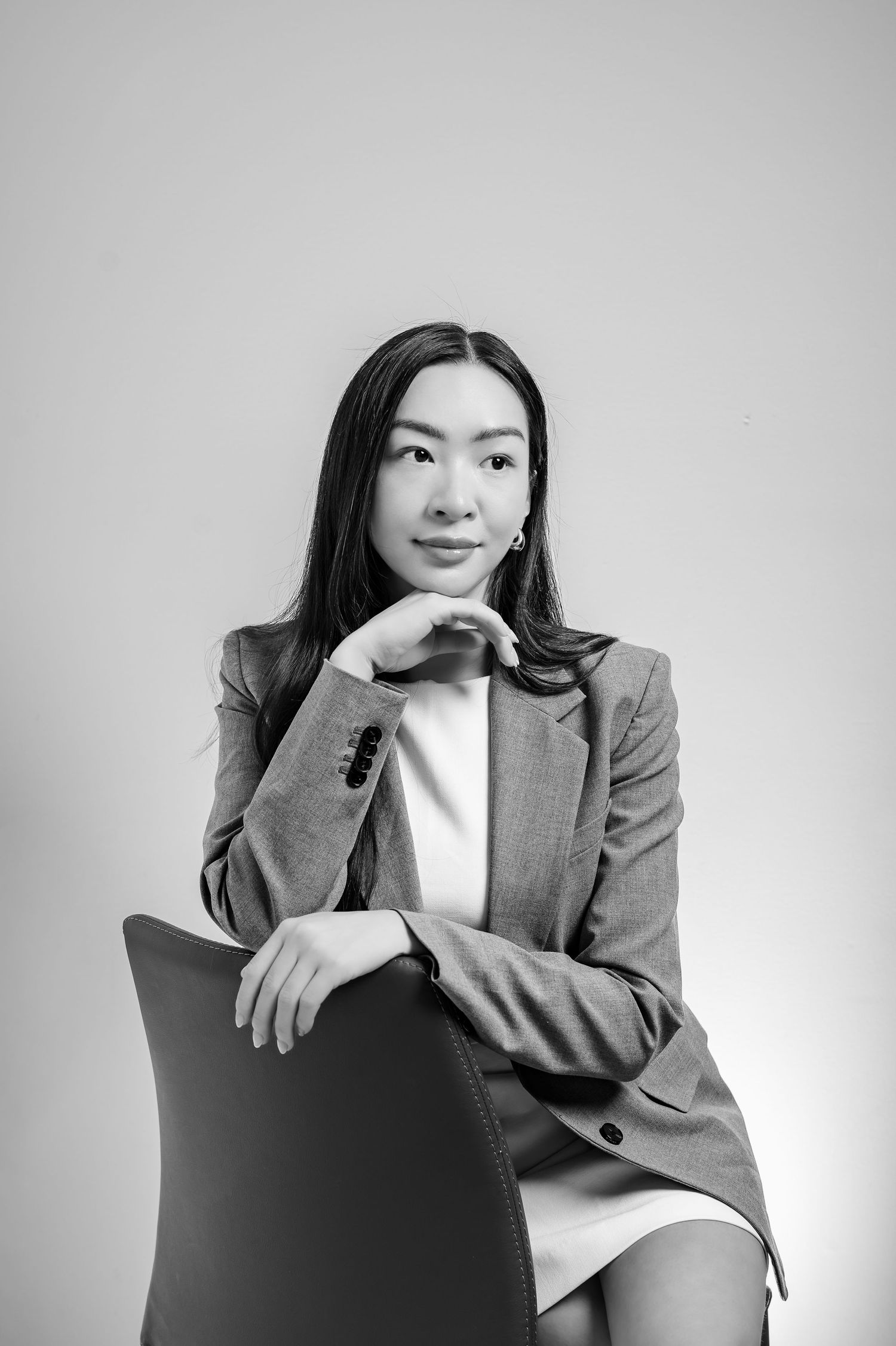 Black and white professional portrait of a young woman in a blazer sitting confidently on a chair.