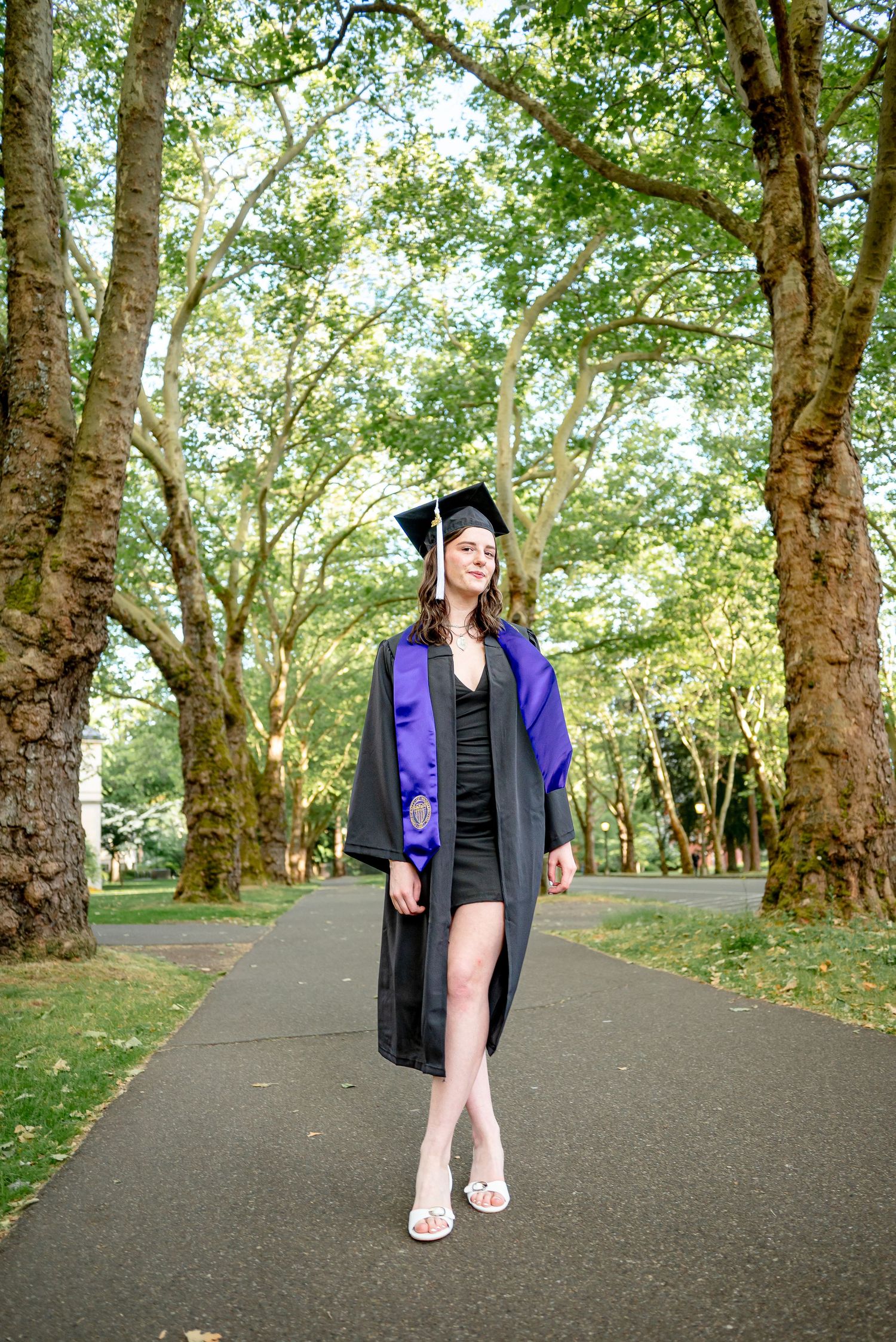 University of Washington graduate walking beneath trees during a golden hour graduation session