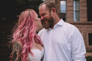 Tattooed bride with pink hair and bearded groom share a romantic moment at their outdoor wedding.