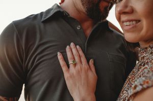 Close-up of woman showing off engagement ring while embracing her partner outdoors.
