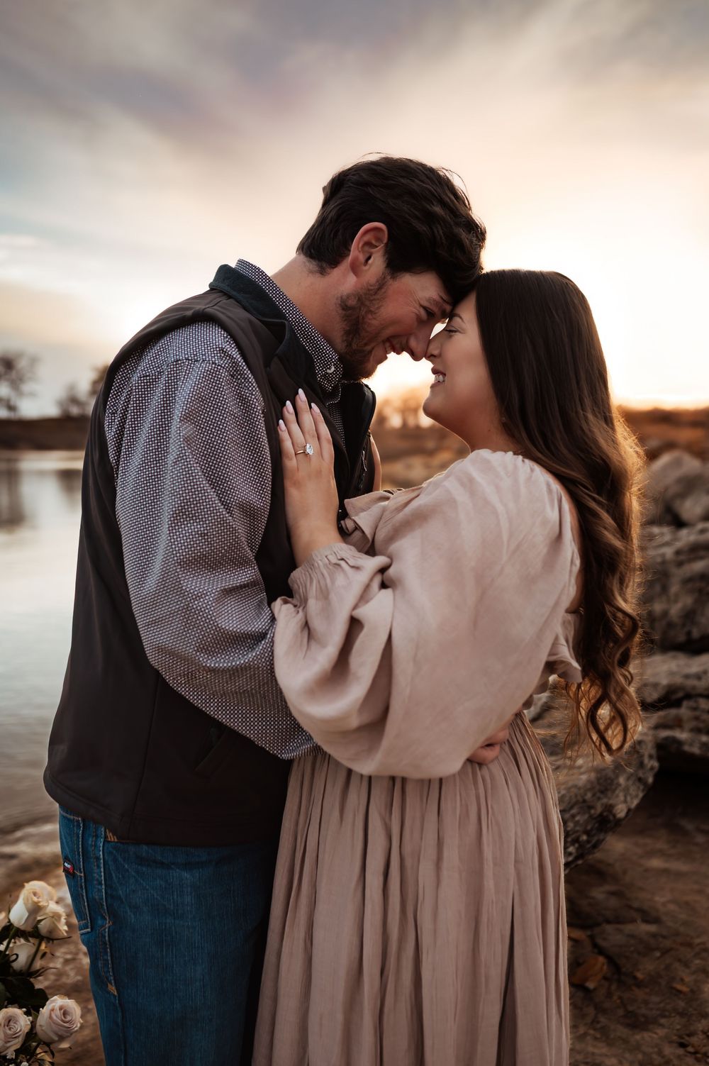 Romantic couple touches foreheads at sunset near a lake during engagement photo session.