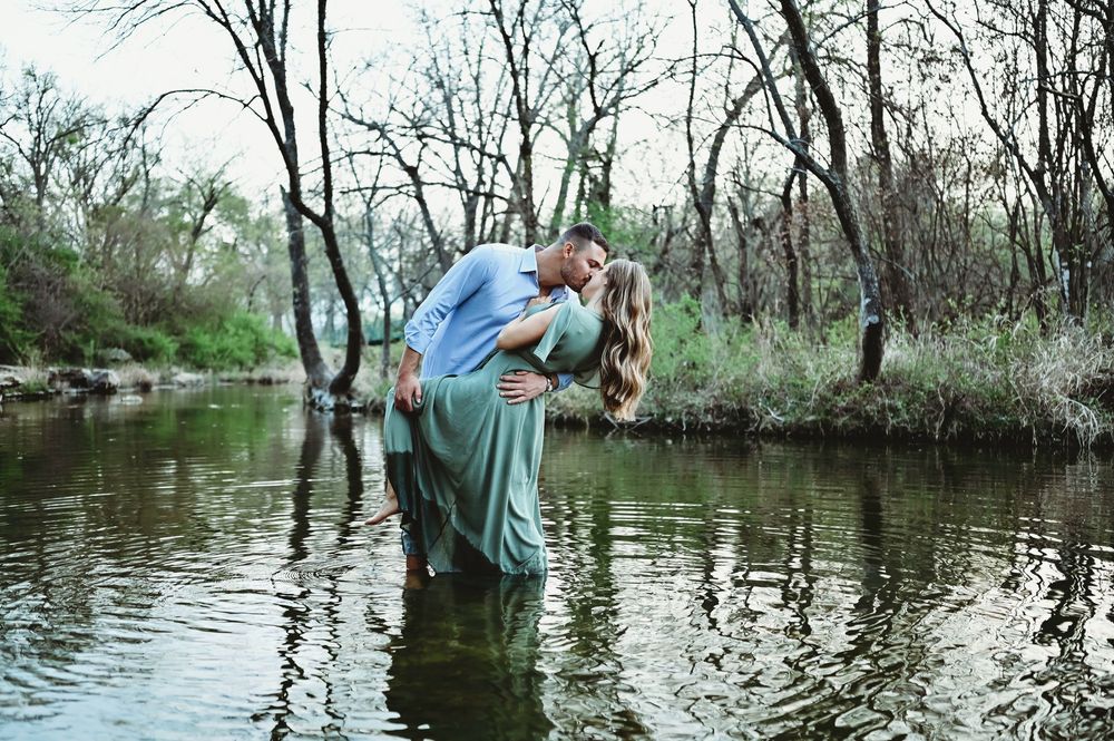 Couple sharing a passionate kiss while standing in a calm river surrounded by bare trees.