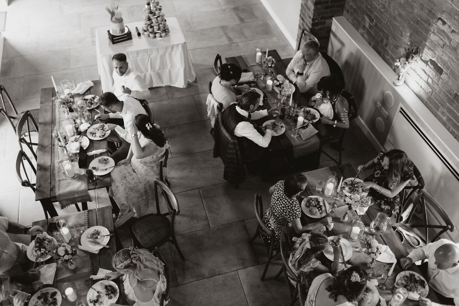 Aerial black and white photo of diners eating at tables in a rustic wedding breakfast with stone walls.