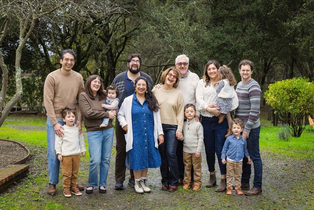 Large multigenerational family smiling together outdoors in a lush green park setting for a portrait.