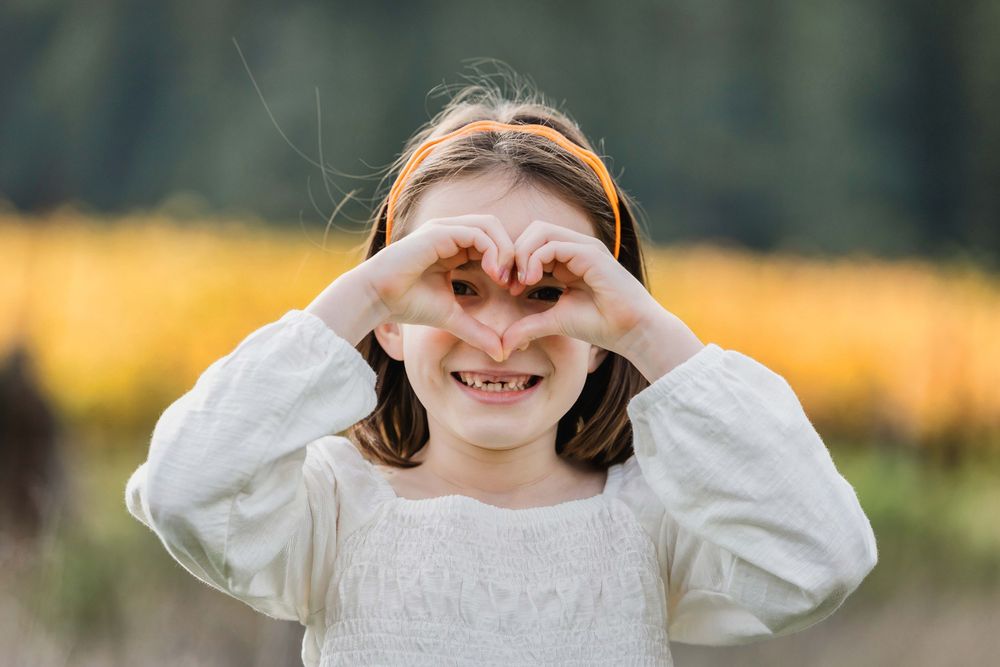 Cute young girl making a heart shape with her hands in an autumn outdoor setting.