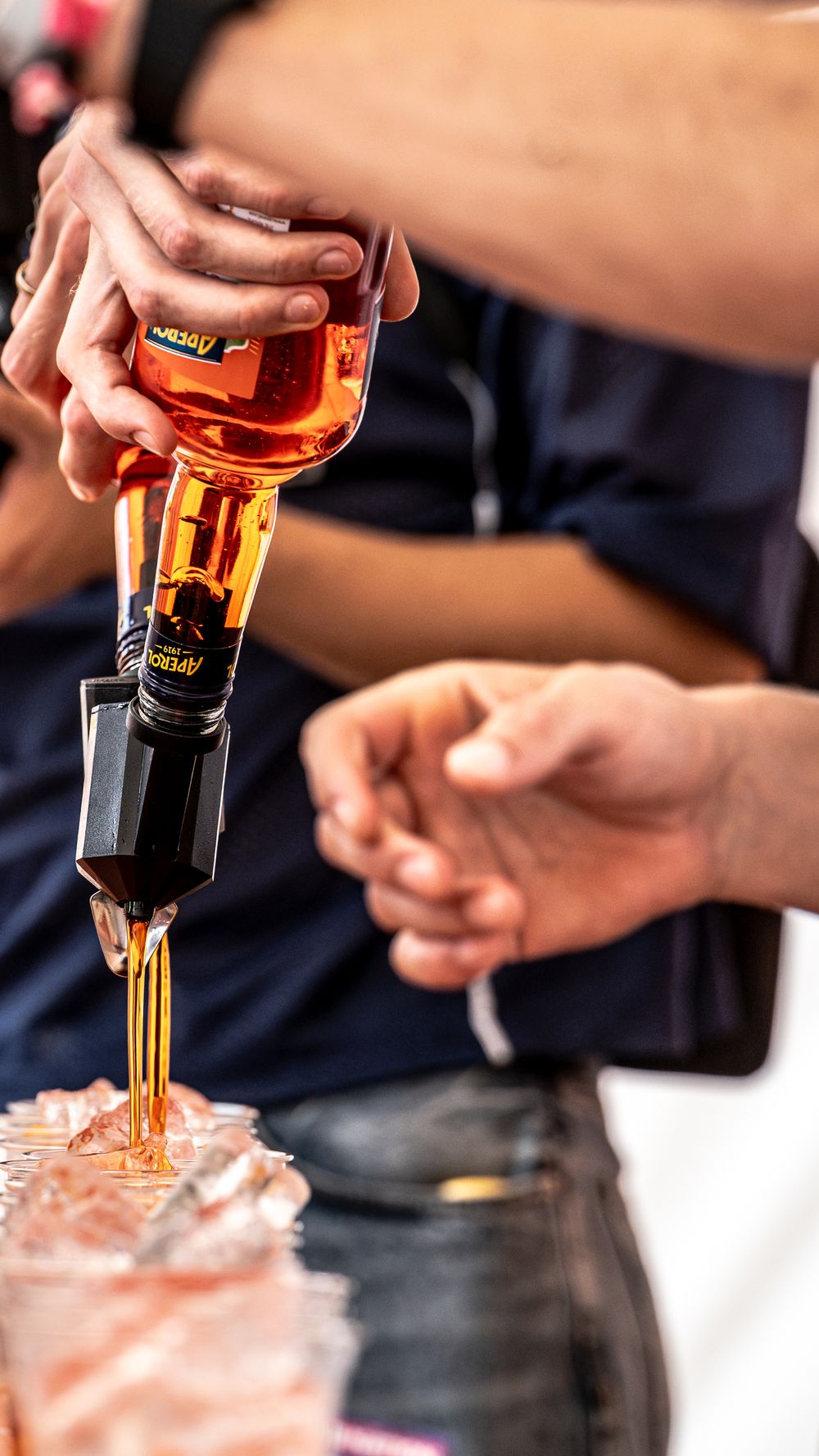 Person pouring amber liquor from a bottle into a glass at a bar event.