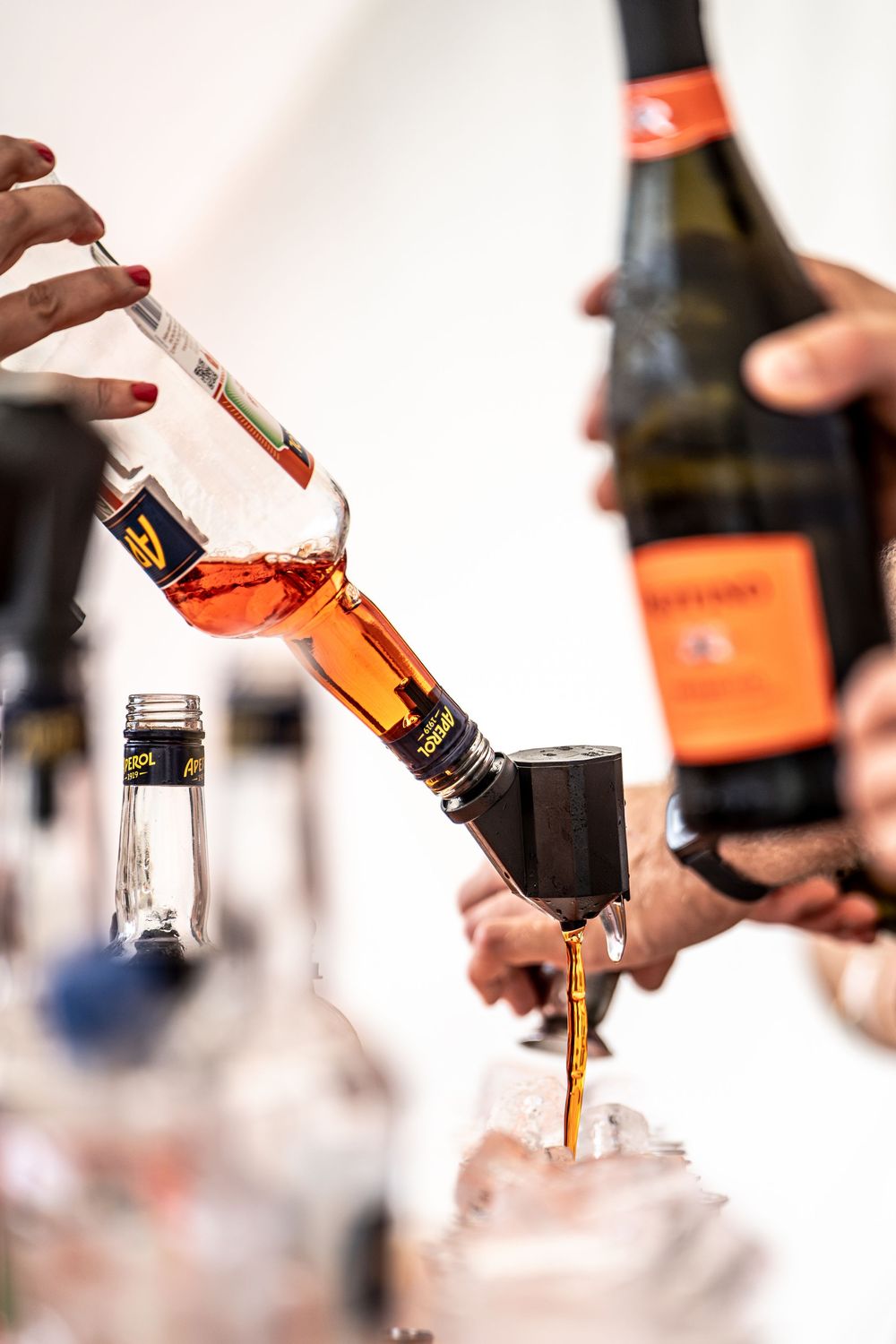 Bartenders pouring amber liquor from bottles into a glass with ice at a bar event.
