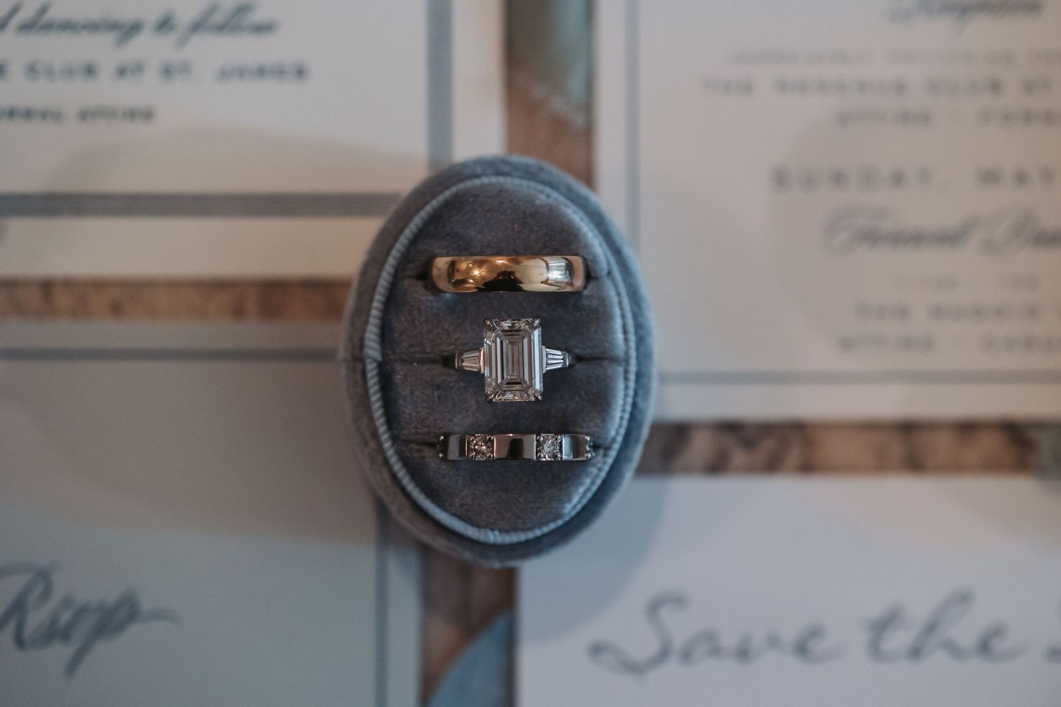 Elegant wedding rings displayed in a velvet ring box alongside wedding stationery and save the date cards.