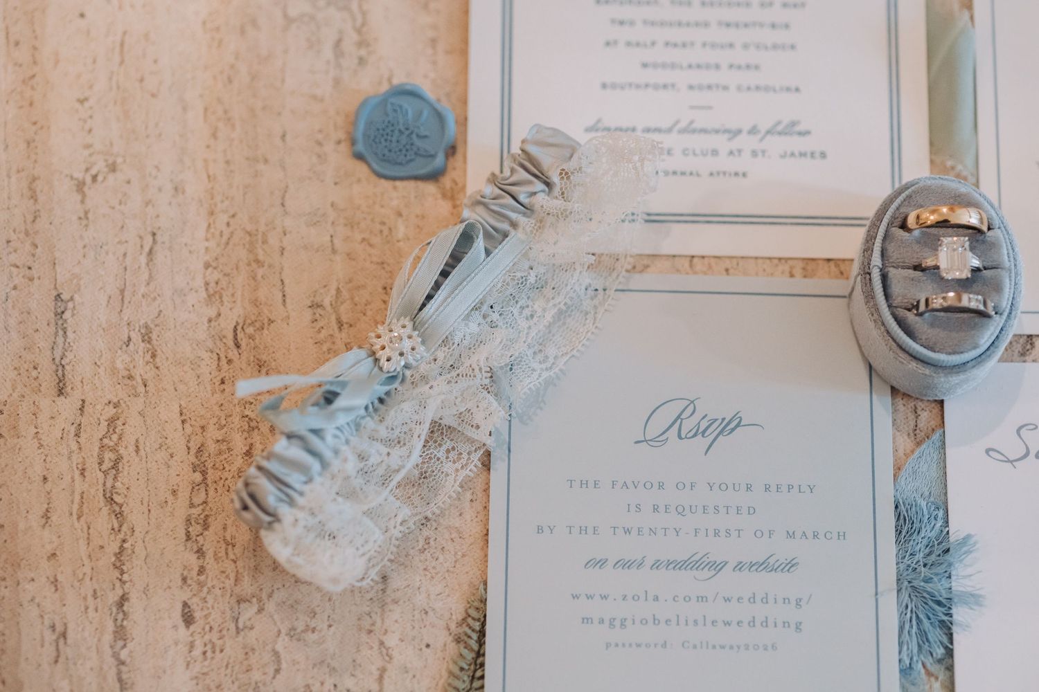 Wedding stationery flat lay with lace garter, diamond rings, RSVP card, and blue wax seals on marble.