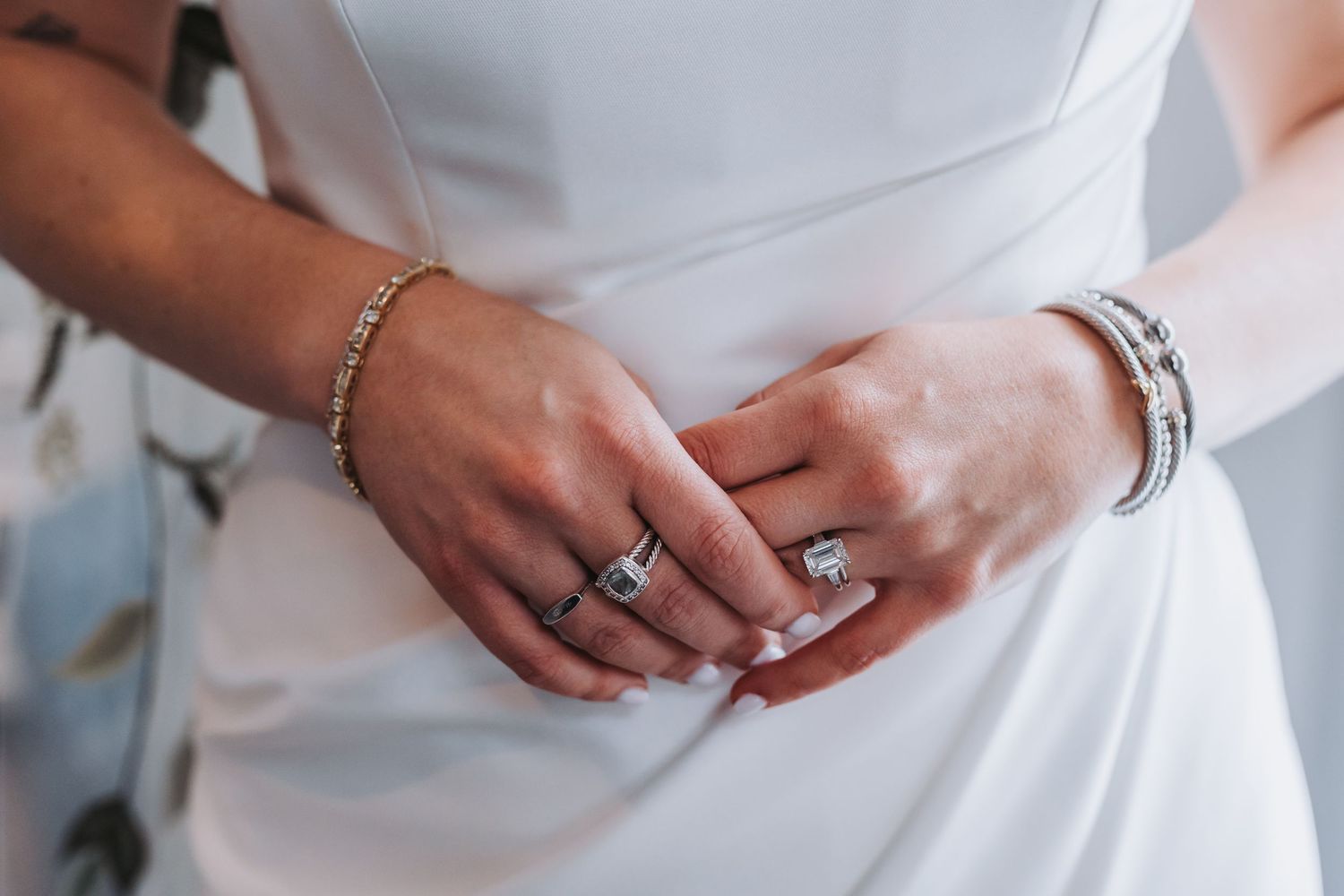 Close-up of bride's hands clasped together wearing diamond engagement ring and silver bracelets.
