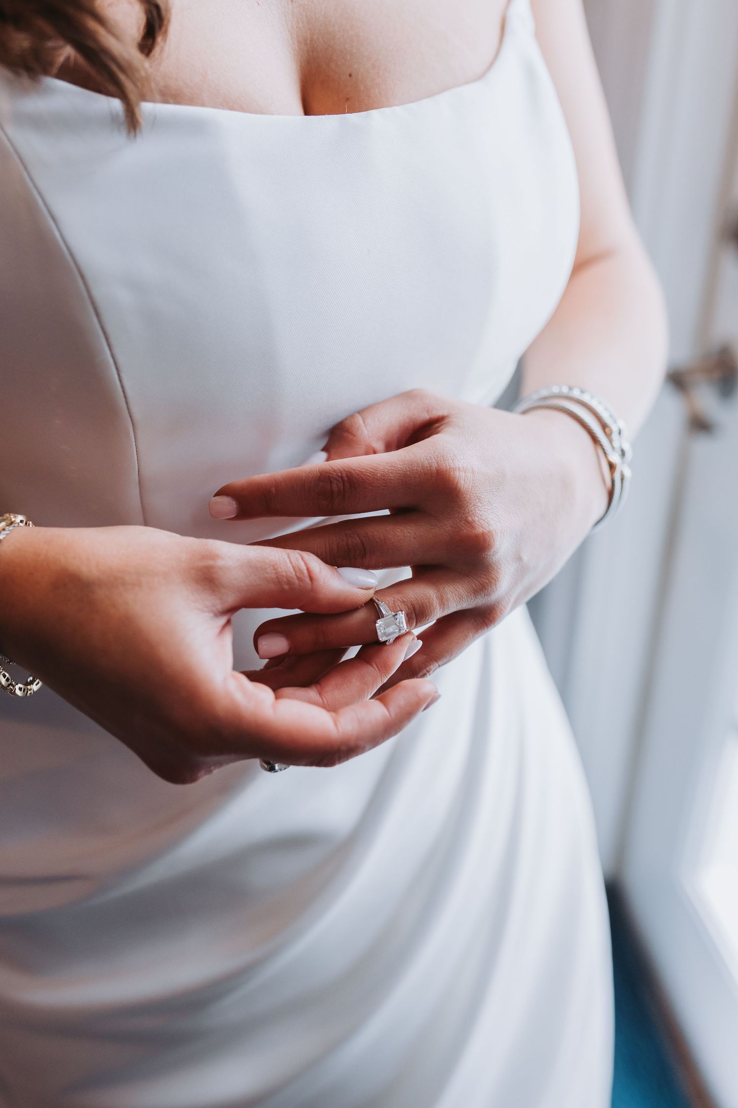Close-up of bride in white dress wearing large diamond engagement ring and delicate silver bracelet.