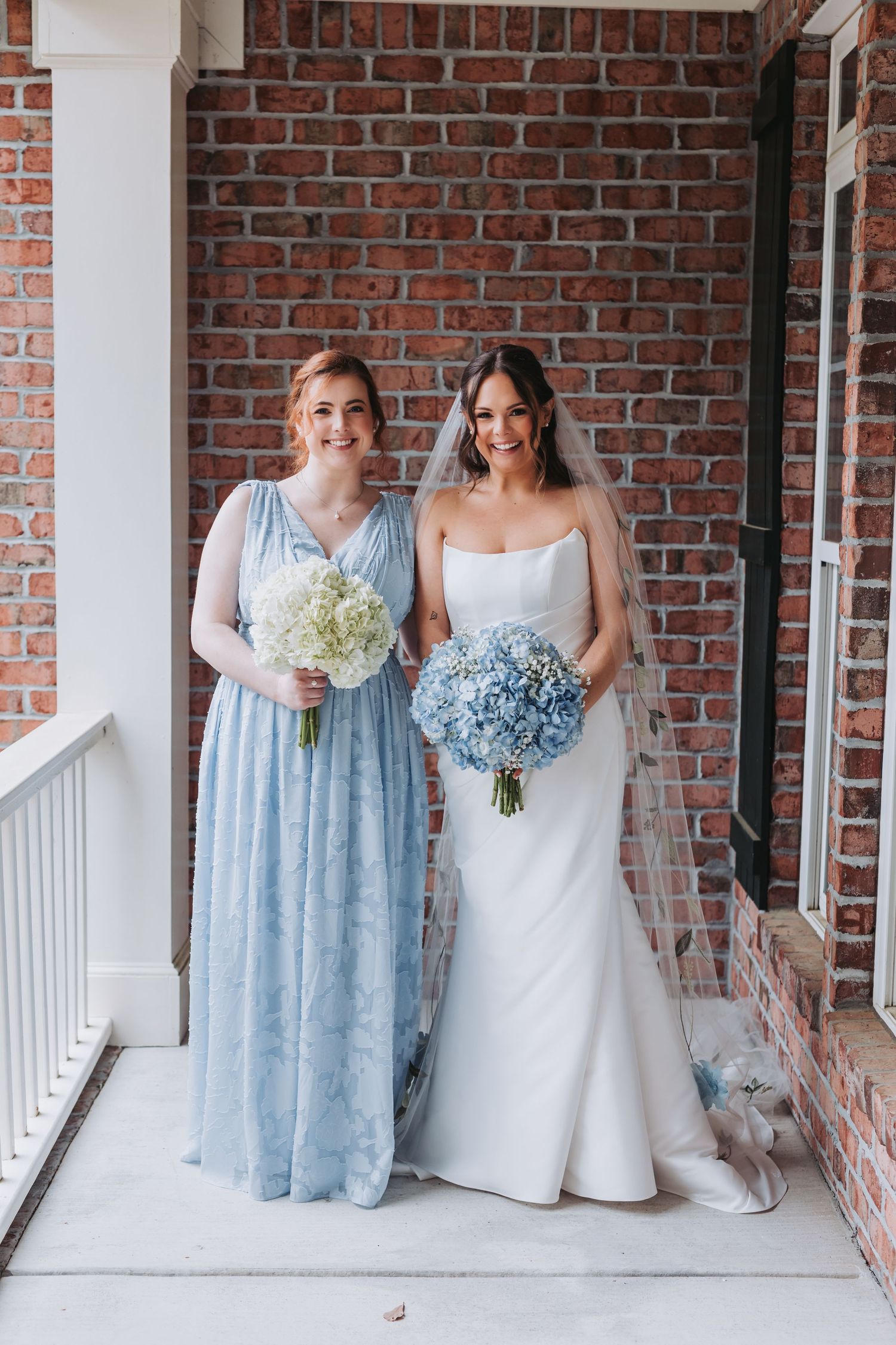 Bride in white strapless gown and bridesmaid in light blue dress holding white and blue hydrangea bouquets.