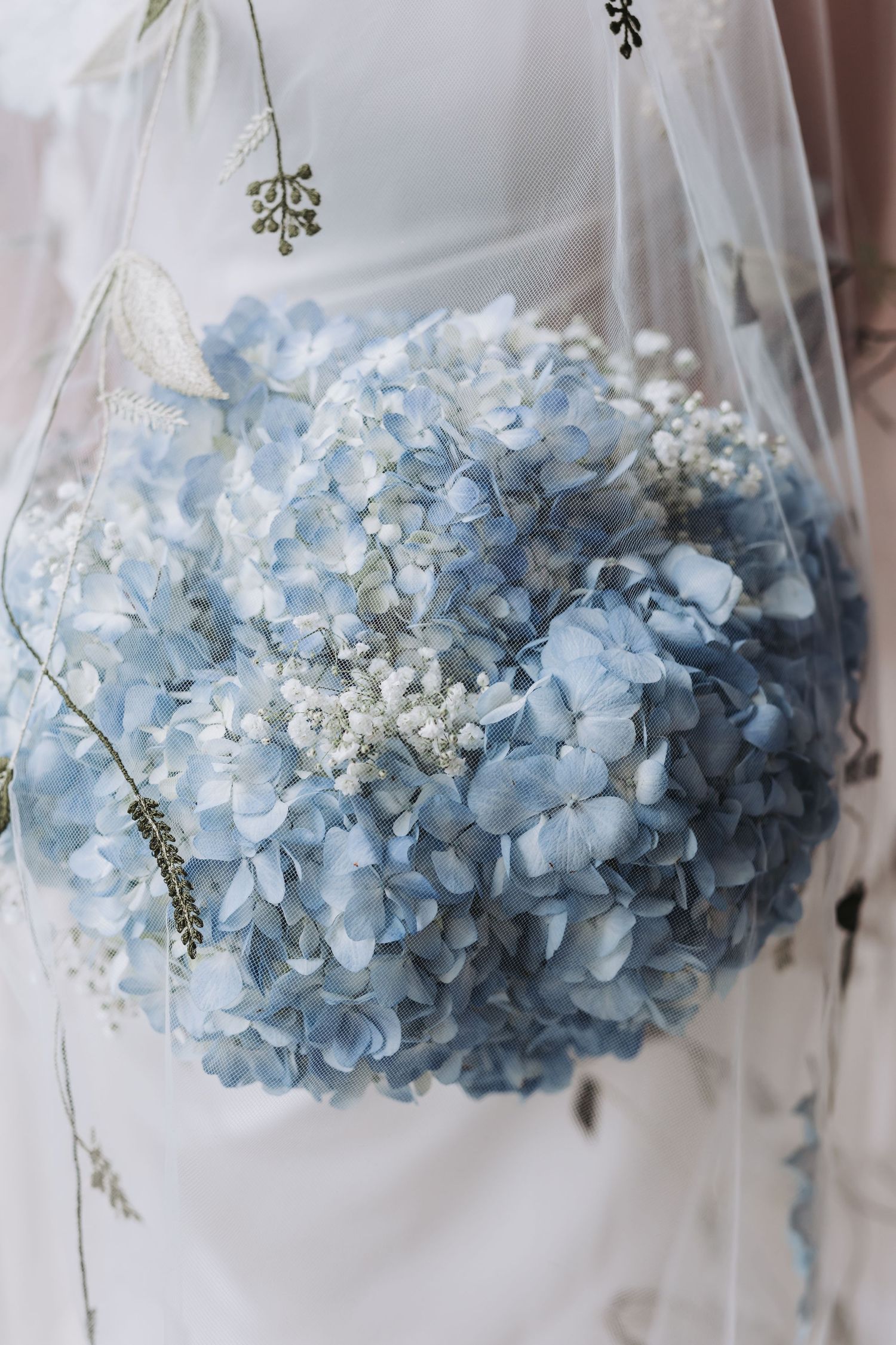Blue hydrangea and baby's breath bridal bouquet draped with a delicate embroidered wedding veil.