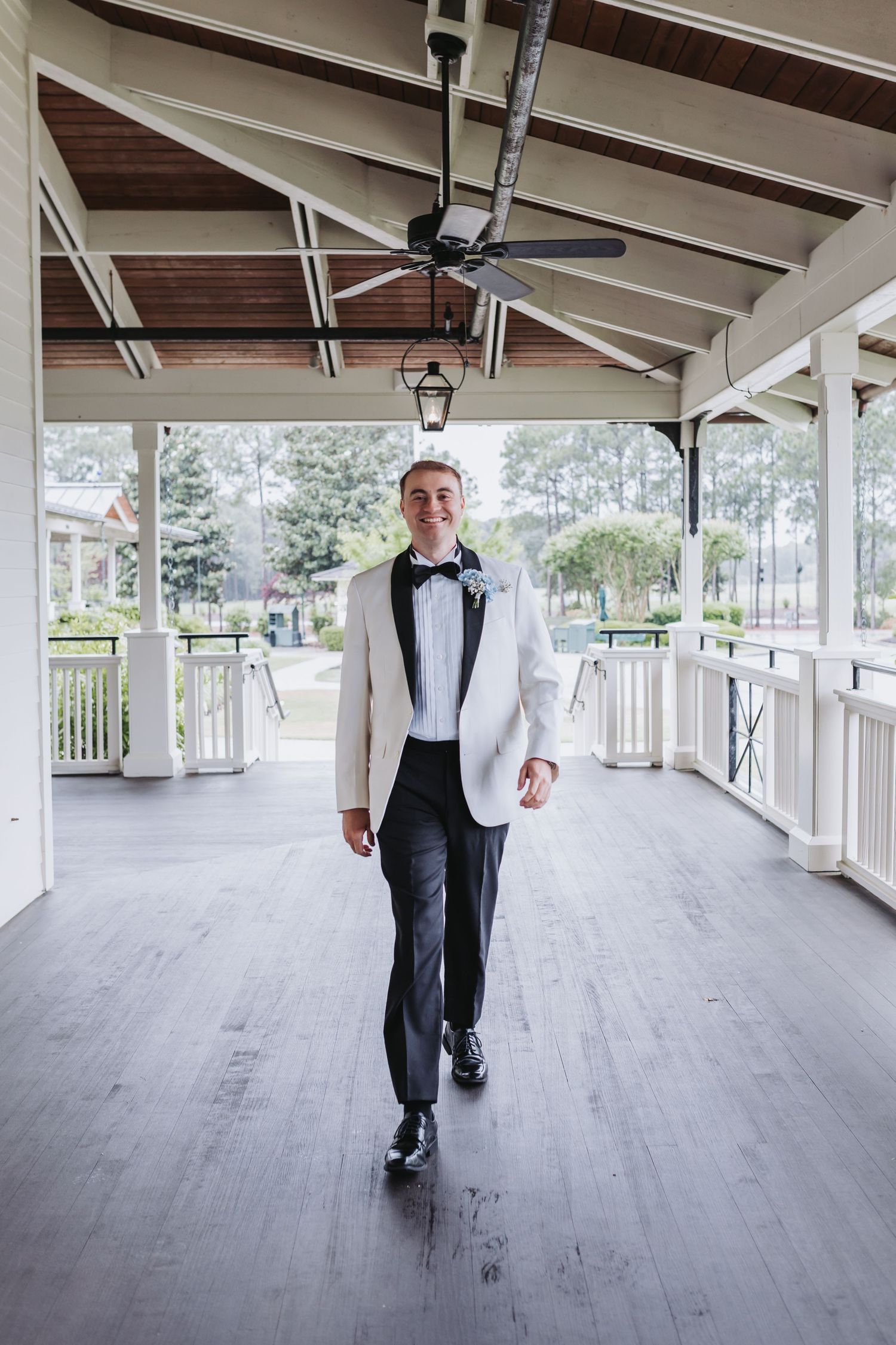 Groom in white tuxedo jacket and black bow tie walking on a covered porch.