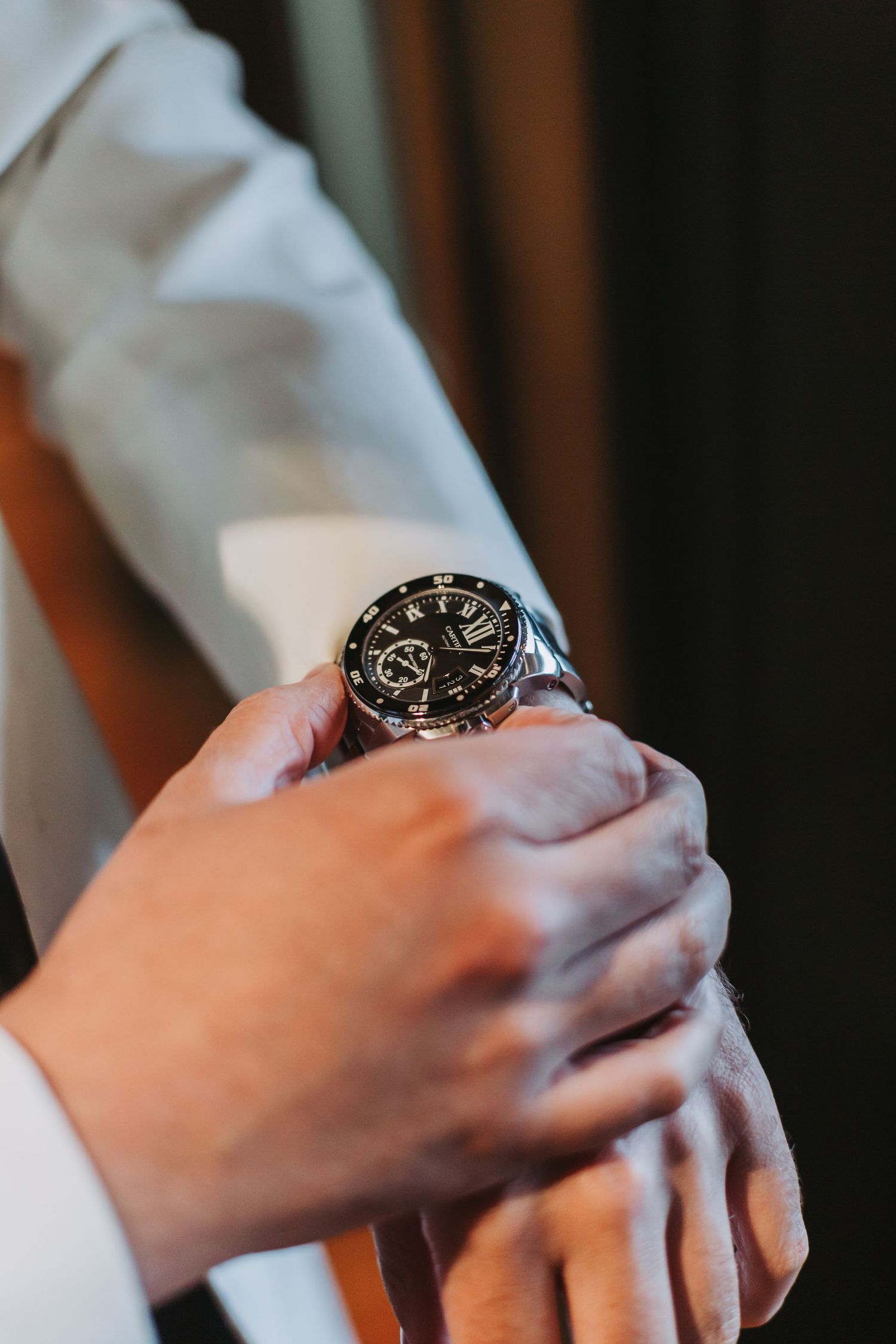 Groom adjusts elegant silver chronograph watch on his wrist while dressed in white wedding attire.