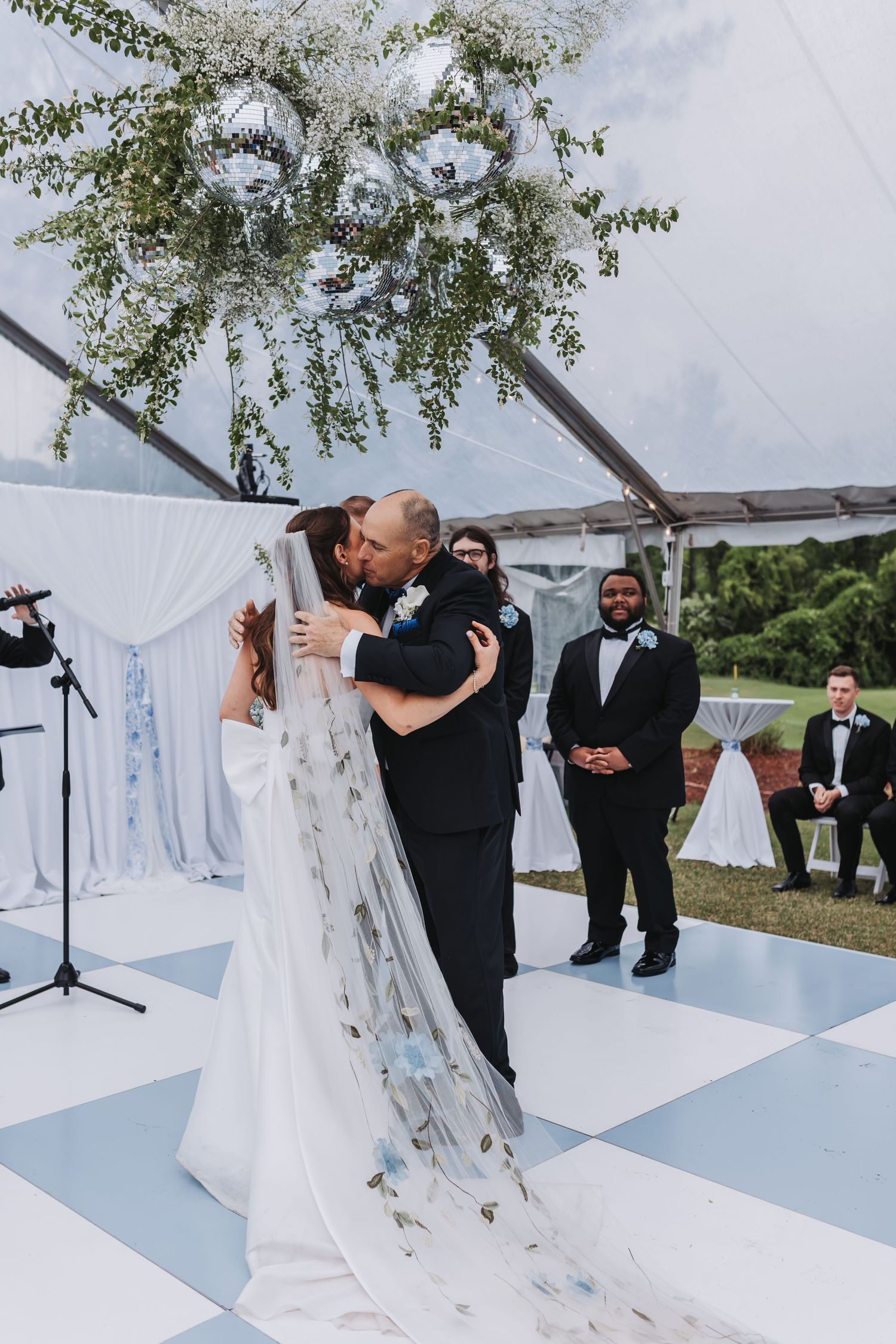 Bride and groom share first kiss at altar under floral chandelier in elegant tented wedding venue.