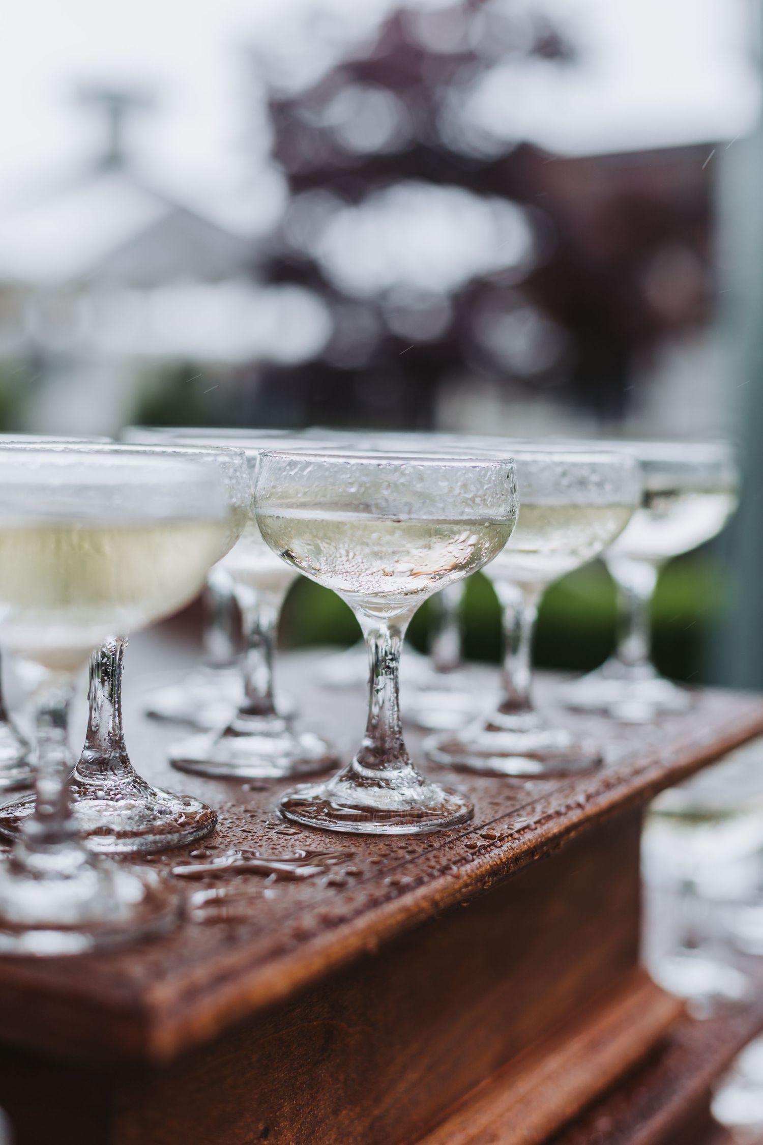 Elegant champagne coupe glasses filled with sparkling wine arranged on a rustic wooden surface at an outdoor wedding reception.