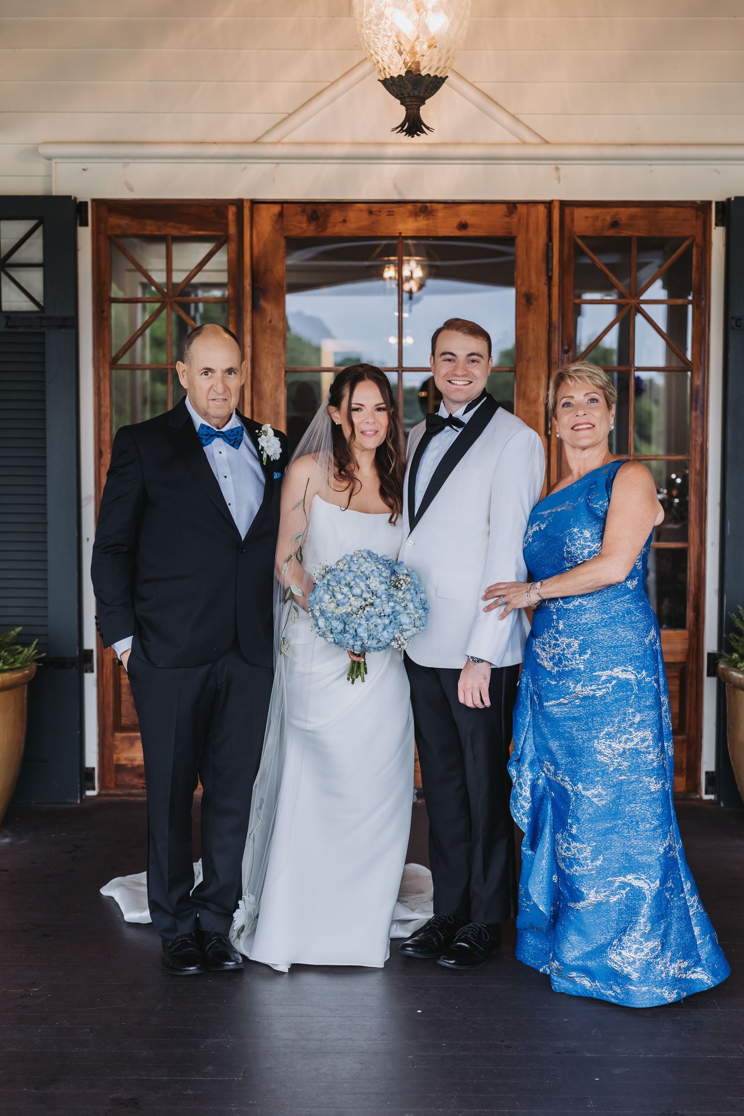 Wedding party of four posing at venue entrance, bride holding blue hydrangea bouquet.