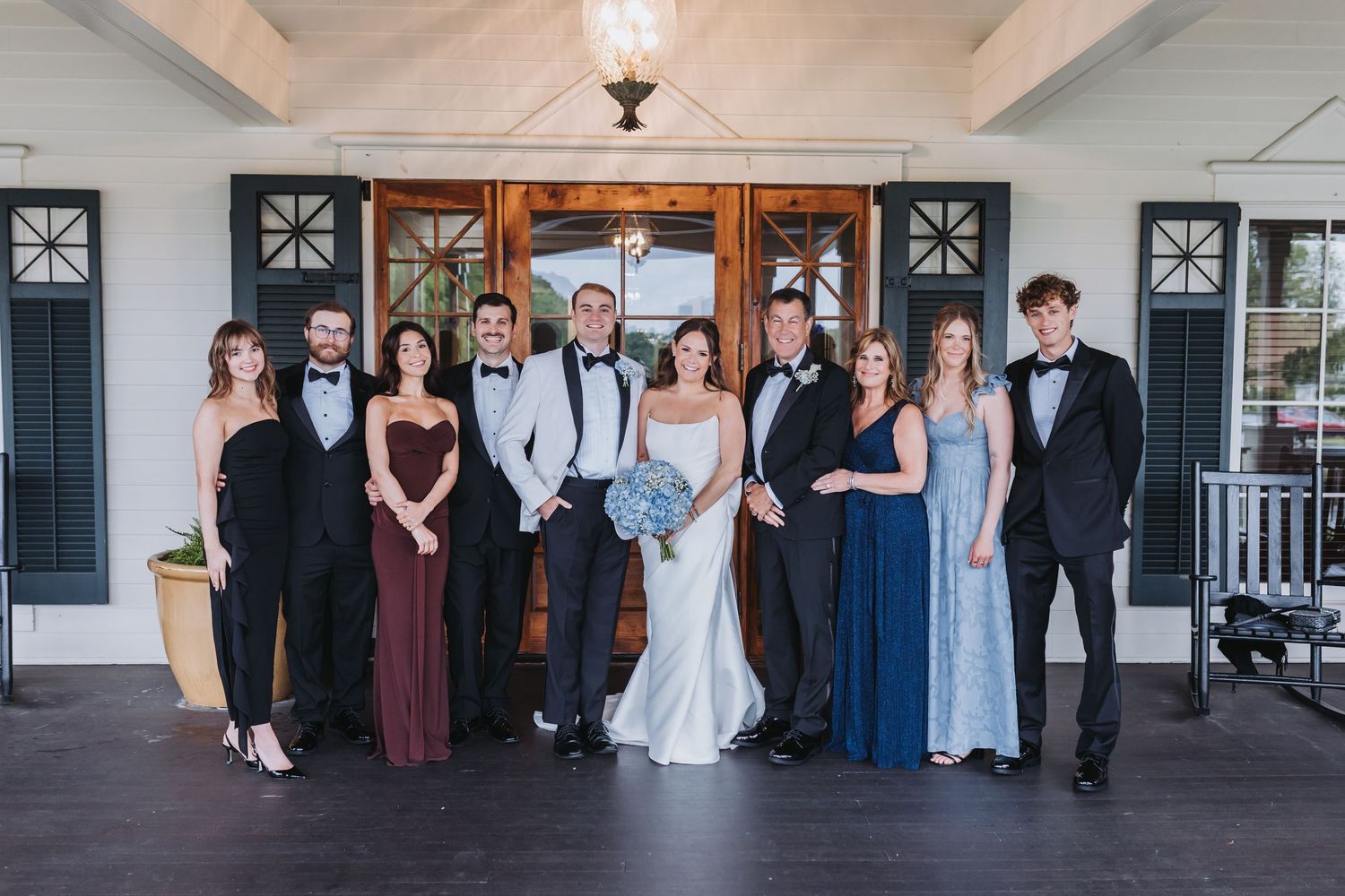 Wedding party poses in formal attire before elegant venue entrance with wooden doors.