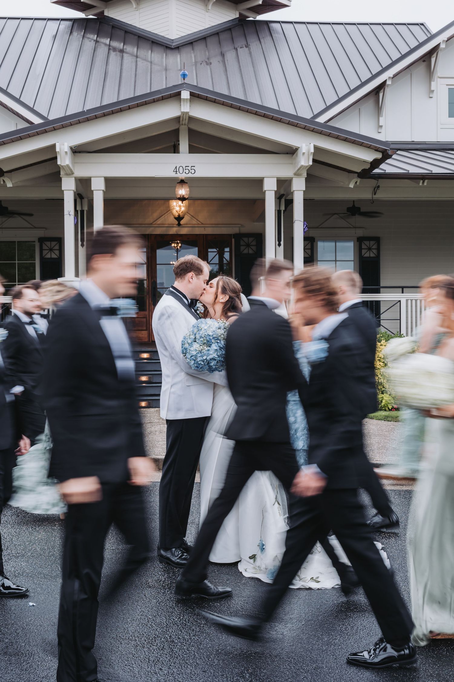 Bride and groom share romantic kiss as wedding party moves around them in motion blur.