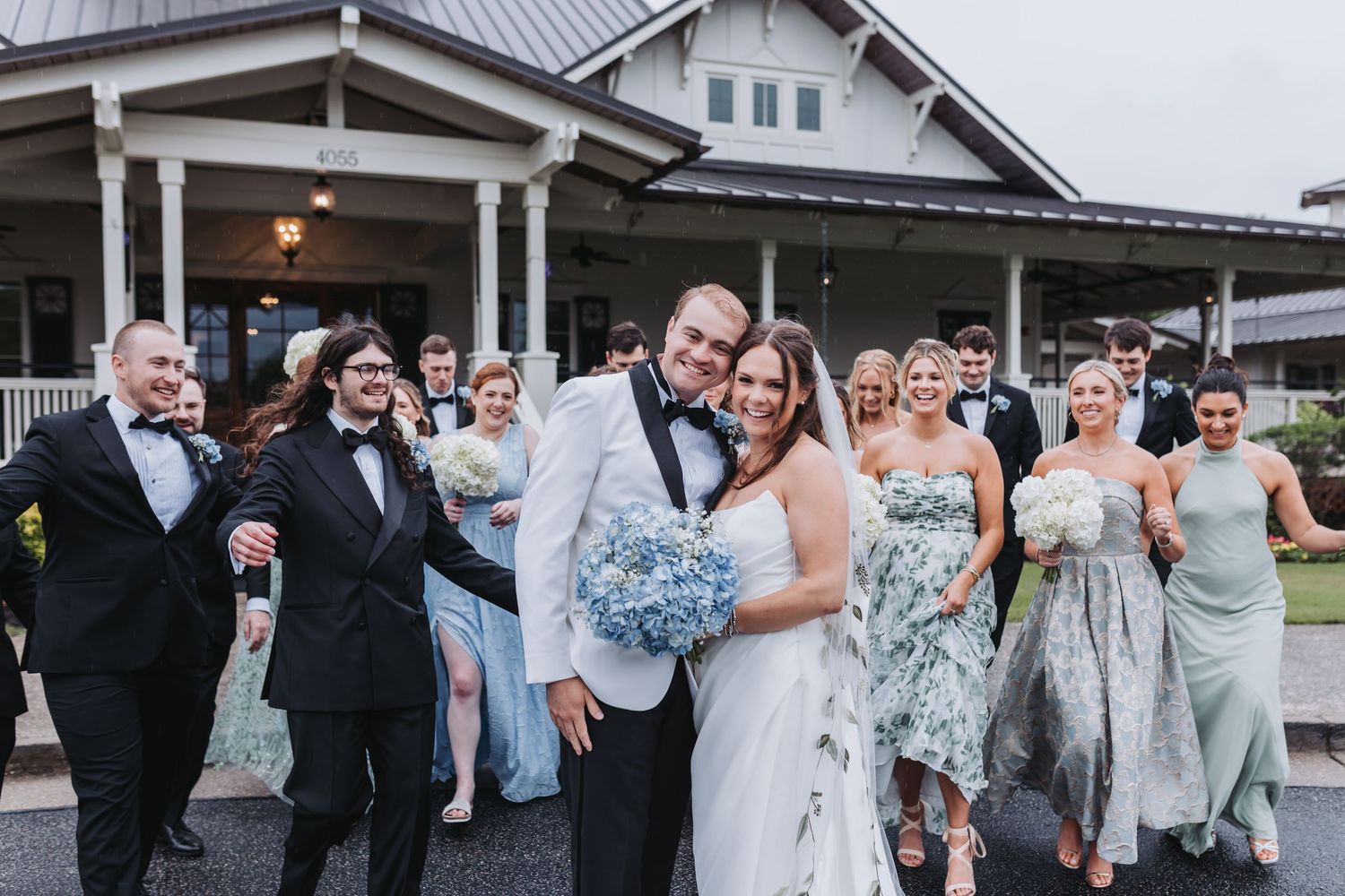 Bride and groom celebrate joyfully with wedding party in blue and black formal attire.