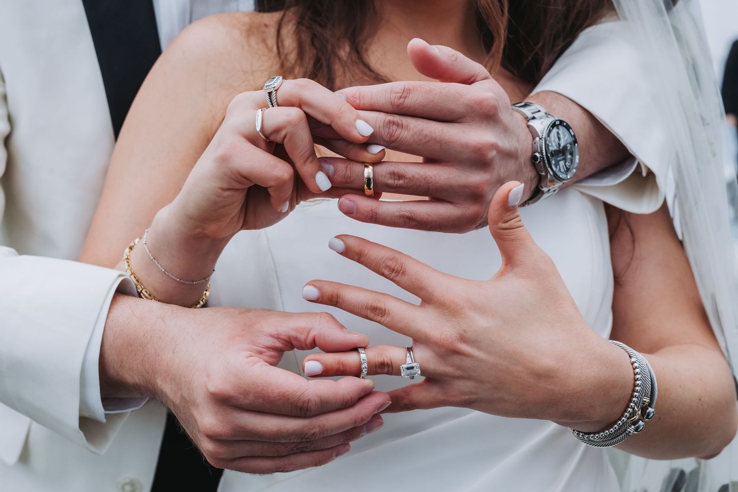 Bride and groom display wedding rings and jewelry on intertwined hands close-up.