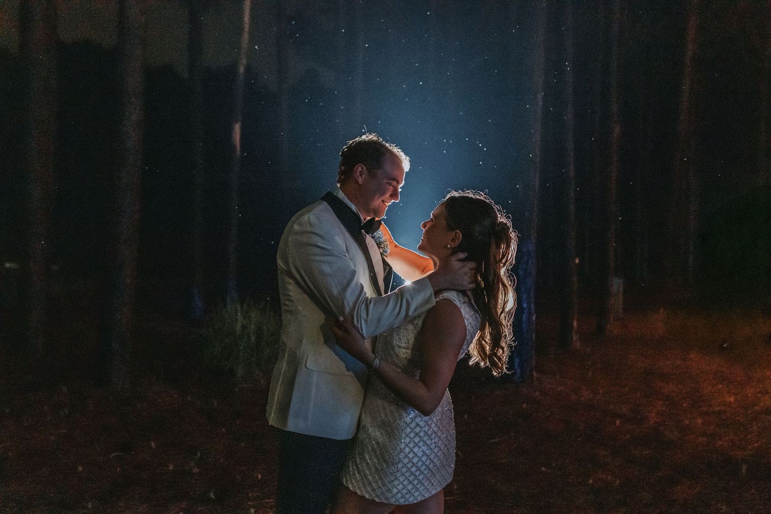 Couple sharing intimate moment together in glowing forest setting during nighttime wedding celebration.