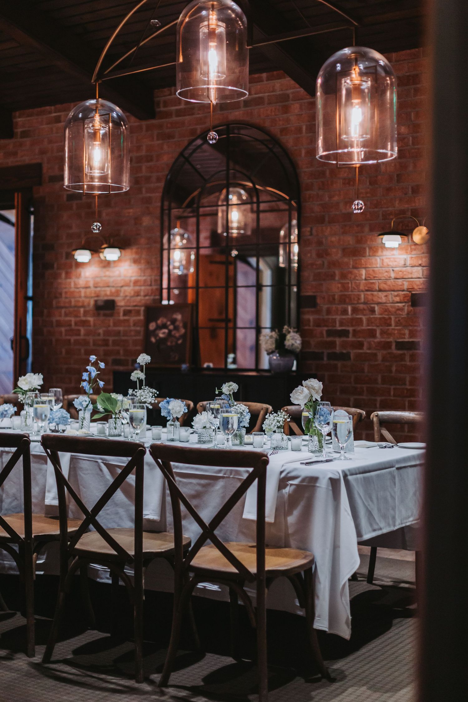 Elegant wedding reception dining room with exposed brick walls, pendant lights, and floral centerpieces.