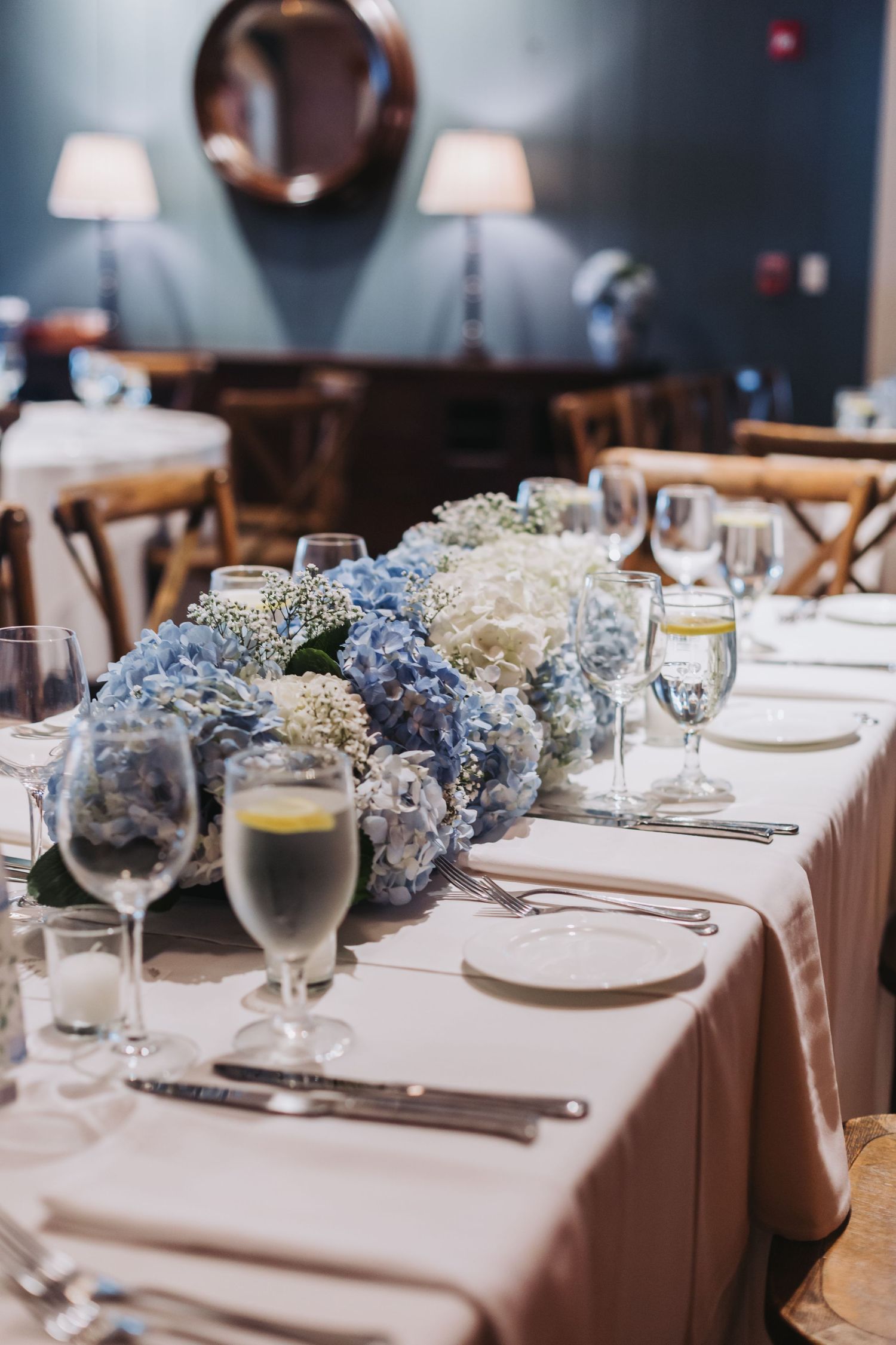 Elegant wedding reception table set with blue and white hydrangea centerpiece and crystal glassware.