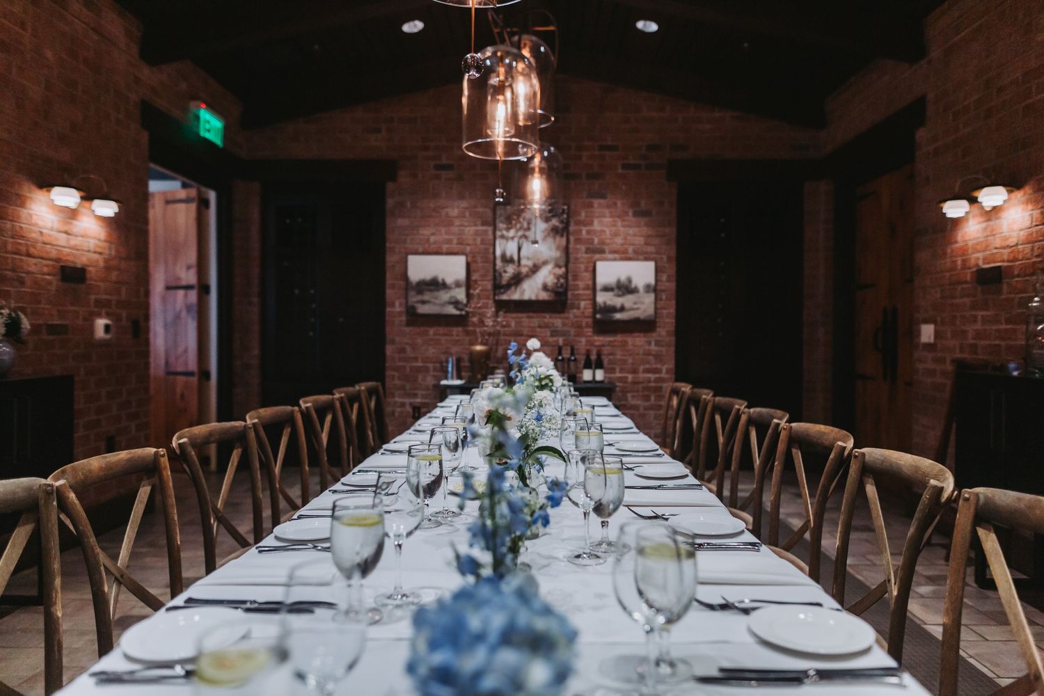 Elegant long dining table set with blue floral centerpieces in a rustic brick room.