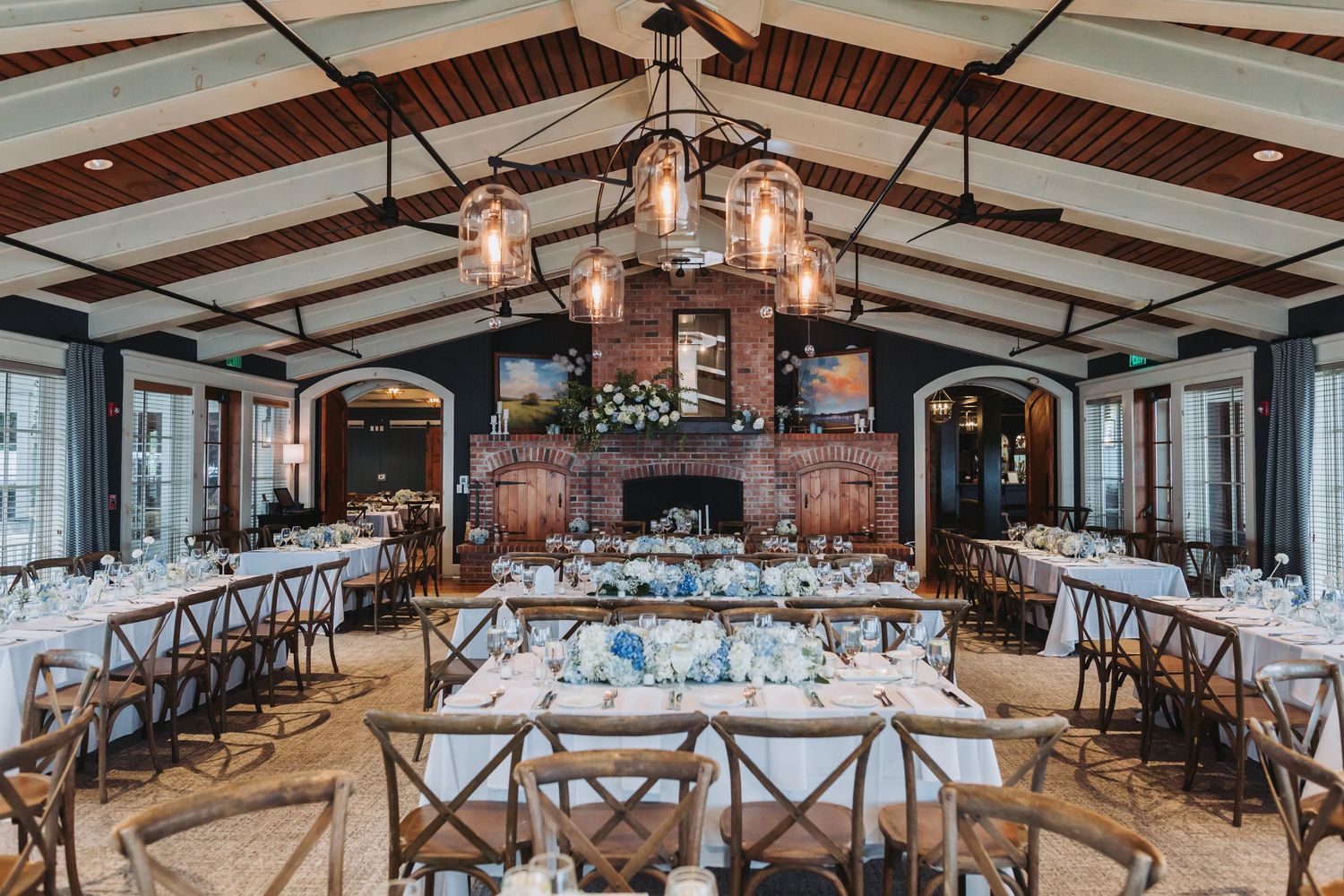 An elegant wedding reception hall with vaulted ceilings, rustic chandelier, and blue and white floral centerpieces.