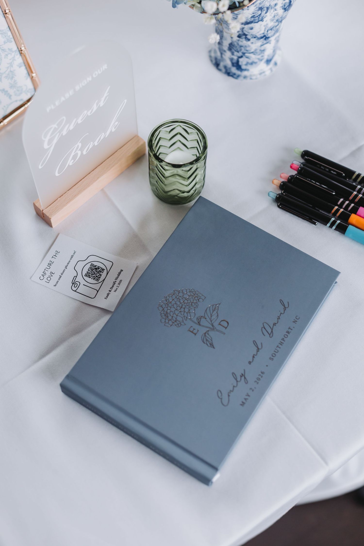 Blue wedding guest book personalized with couple names Emily and David on white linen table.