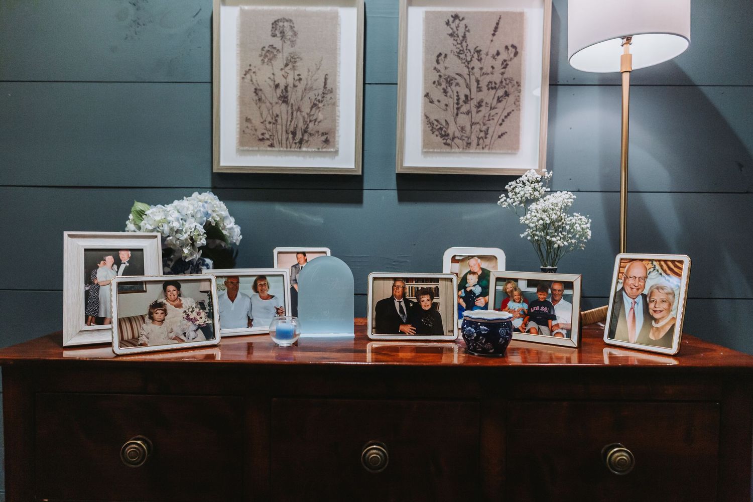 Wedding memory table with framed family photos on a wooden dresser against a teal wall with artwork.