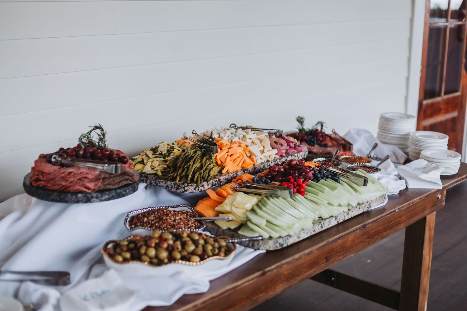 Elegant wedding charcuterie spread with vegetables, meats, and olives on a draped table.