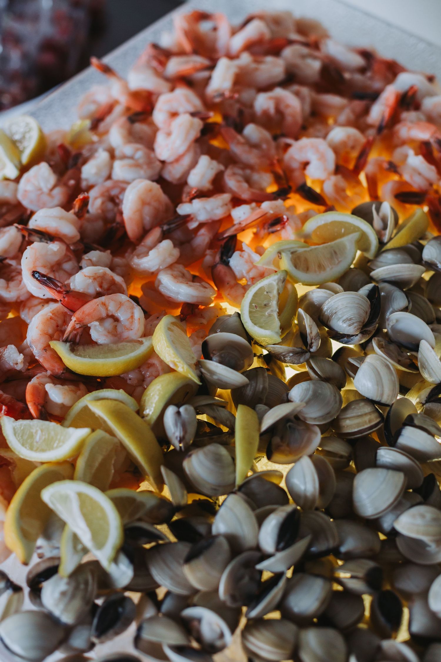 Wedding seafood display with shrimp, clams, and lemon slices on illuminated platter.