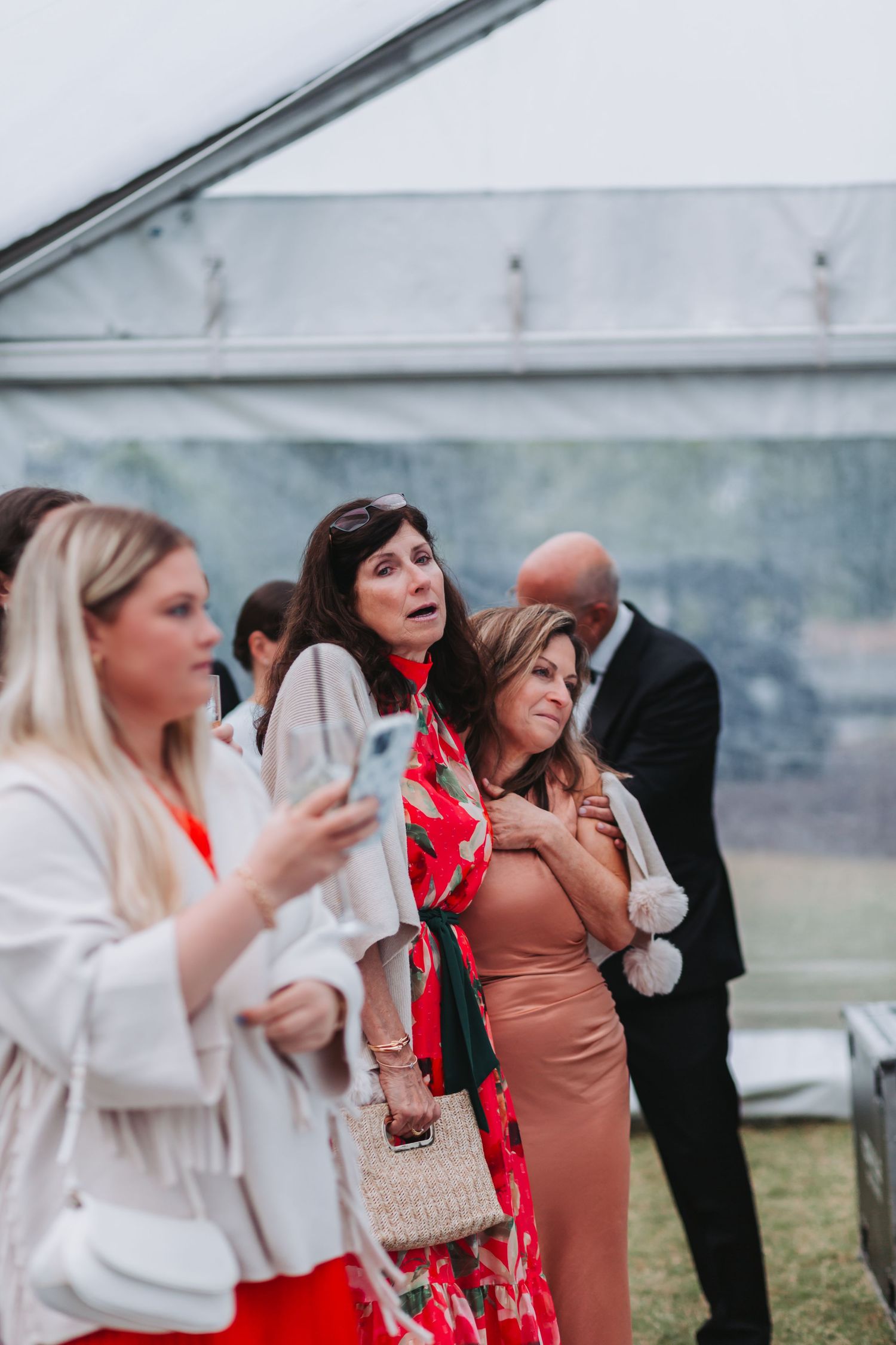 Wedding guests in colorful attire watching ceremony under a clear outdoor reception tent.
