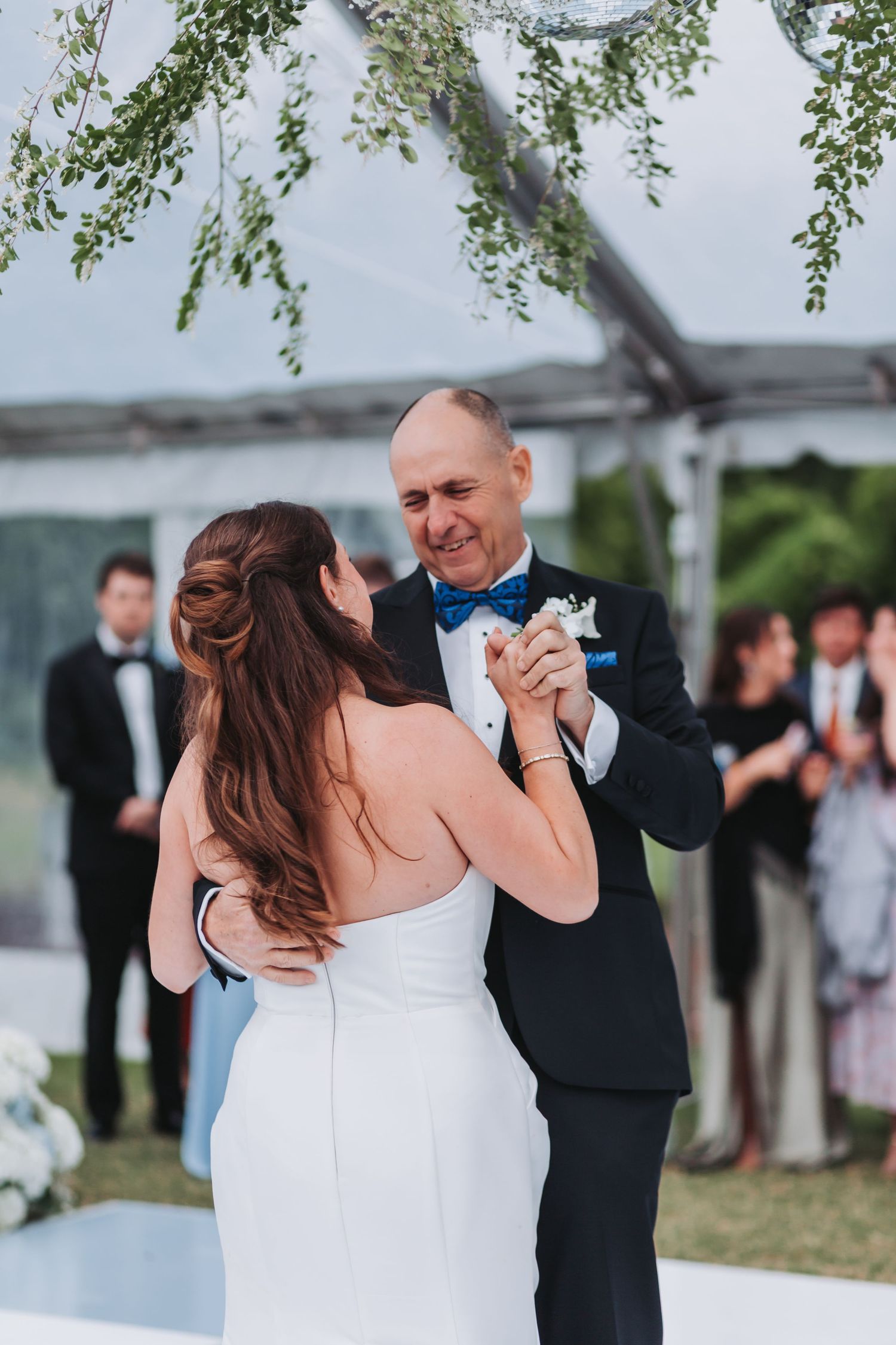 Emotional father-daughter first dance at outdoor wedding reception under a floral decorated tent.