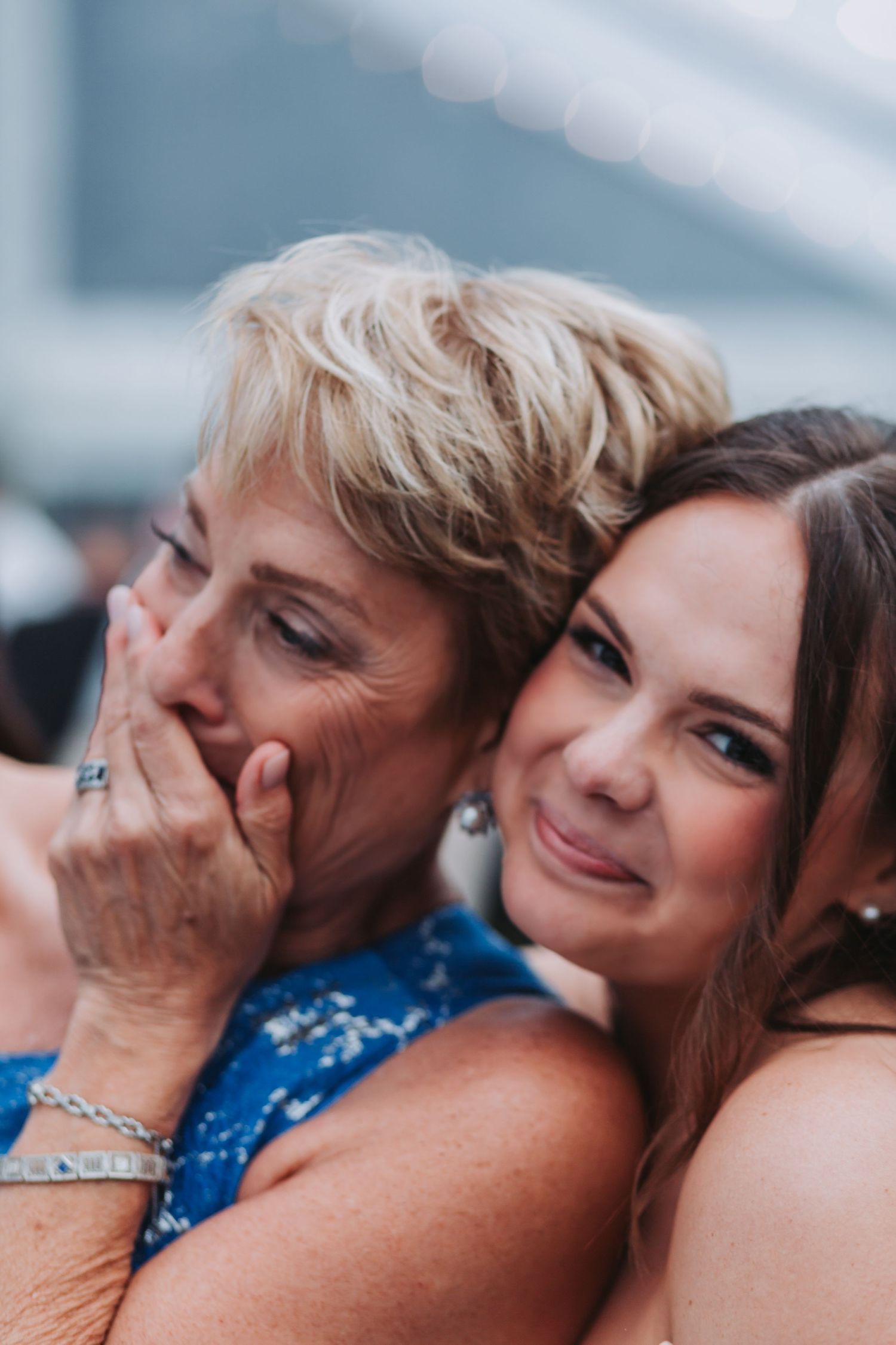 Emotional mother and bride share a tender embrace at wedding reception.