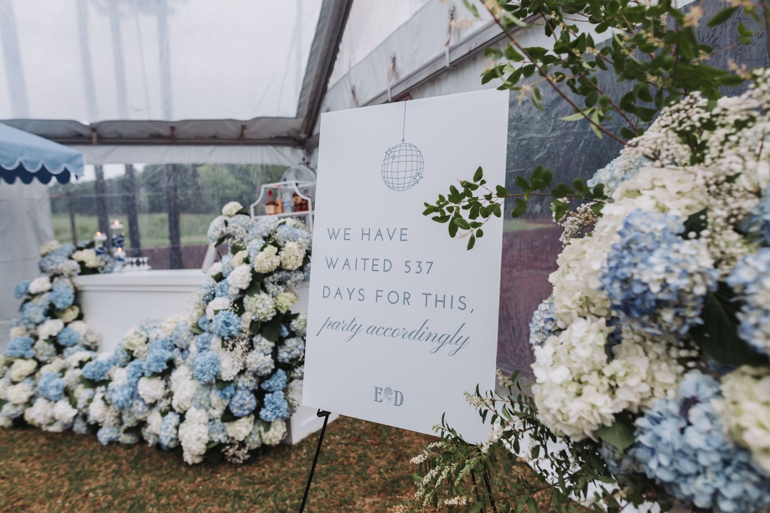Wedding sign surrounded by blue hydrangeas reading we have waited 337 days for this.