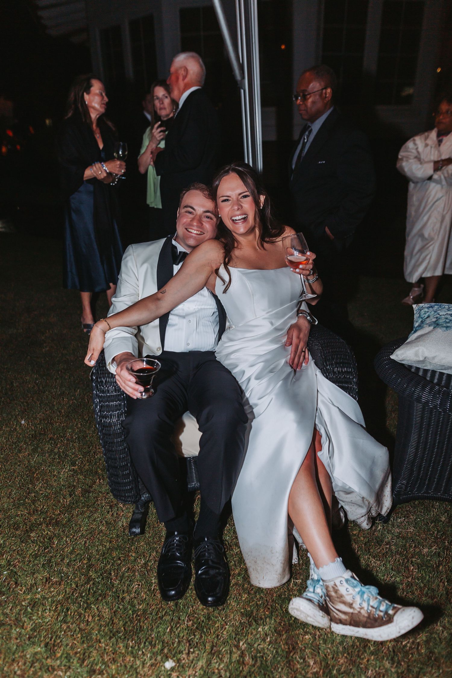 Smiling bride and groom sitting together outdoors at evening wedding reception celebration.