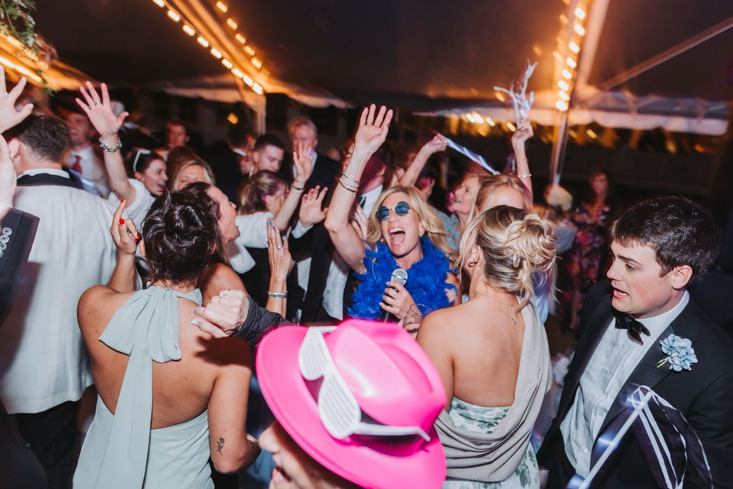 Energetic wedding reception dance floor with guests celebrating under string lights in a festive tent.